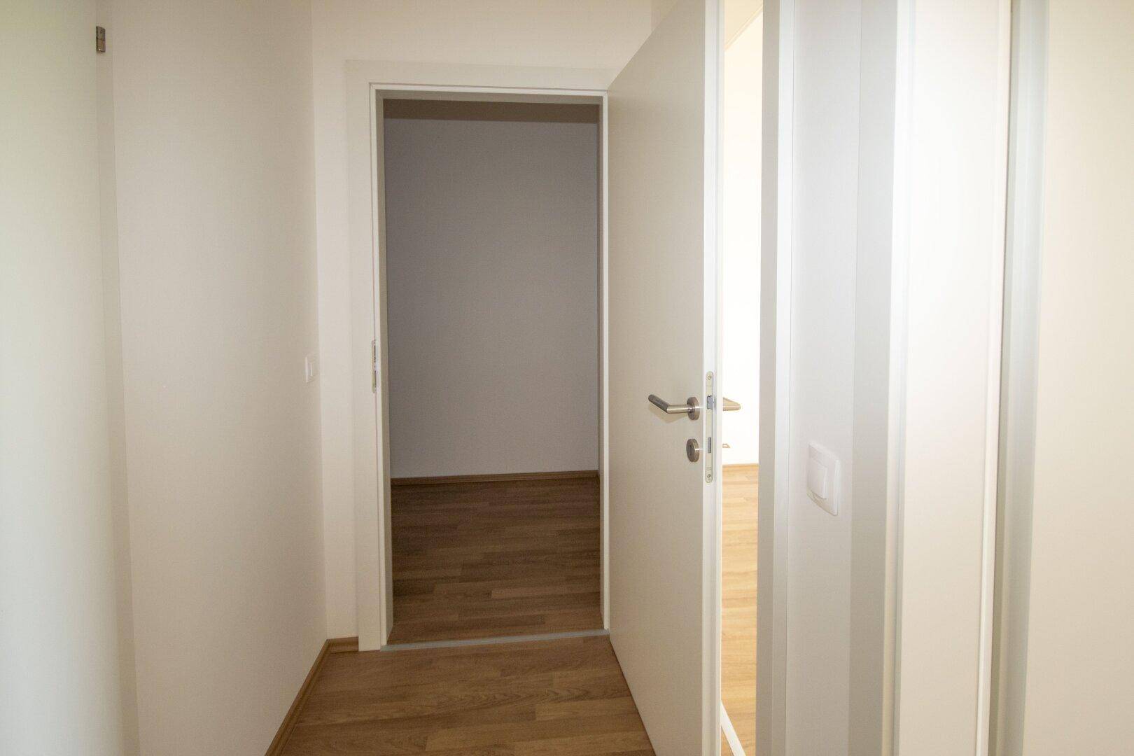 Heller Flur mit Laminatboden und offener Tür, die den Zugang zu einem weiteren Raum ermöglicht.
