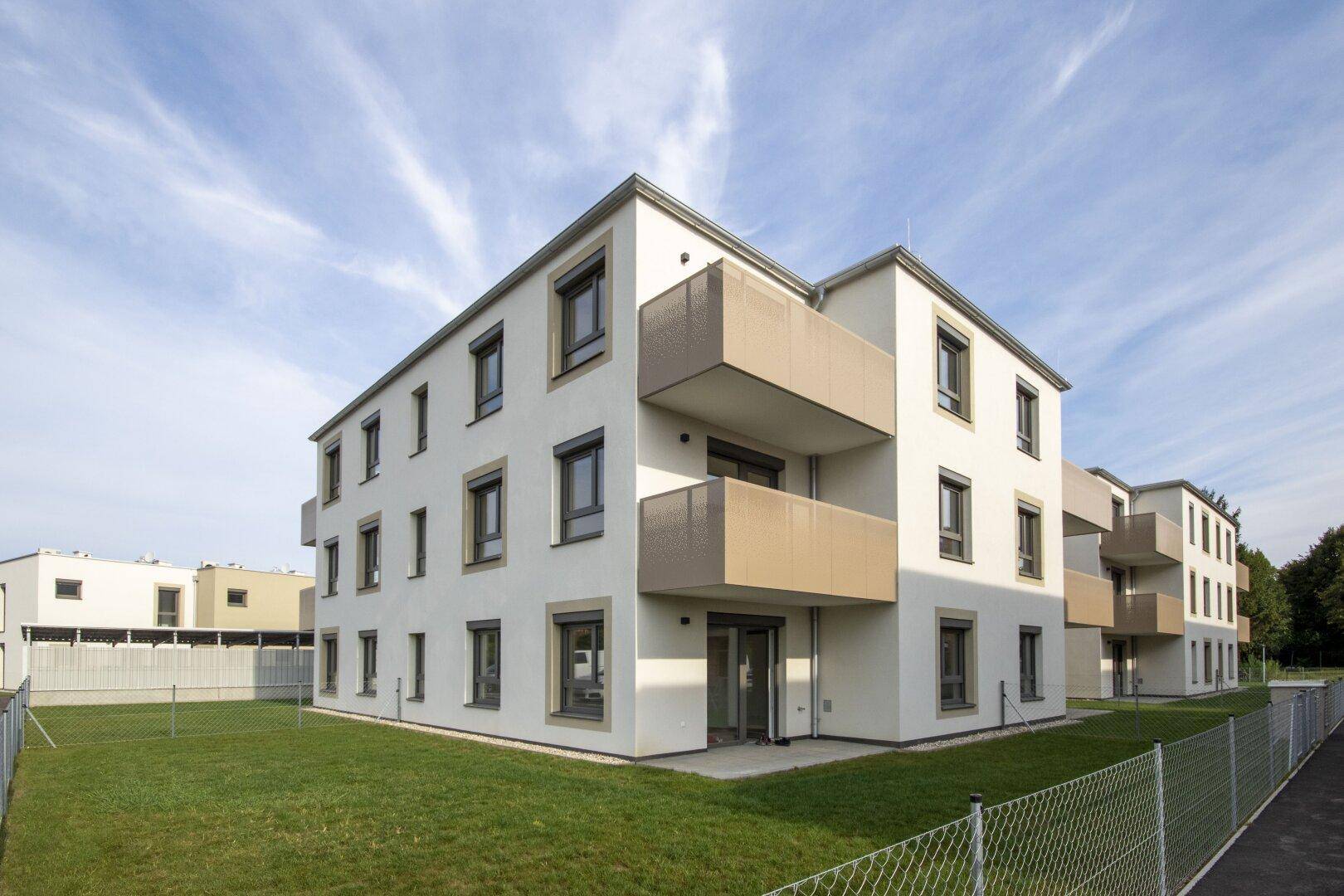 Modernes Mehrfamilienhaus mit weißer Fassade, Balkonen und gepflegter Rasenfläche.