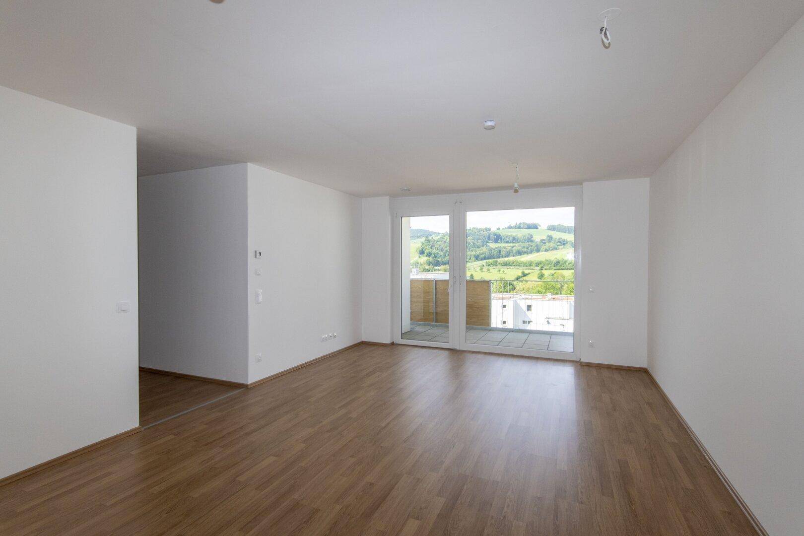 Helles Wohnzimmer mit Holzboden und großem Fenster mit weitem Blick ins Grüne.
