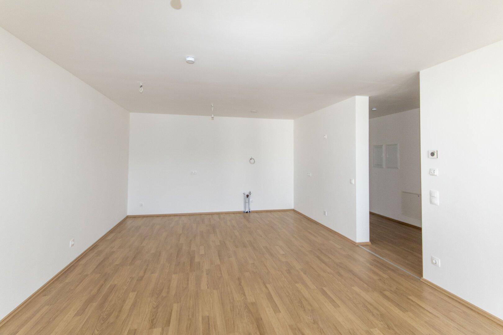 Geräumiger, leerer Wohnbereich mit hellem Holzboden und frisch gestrichenen weißen Wänden.