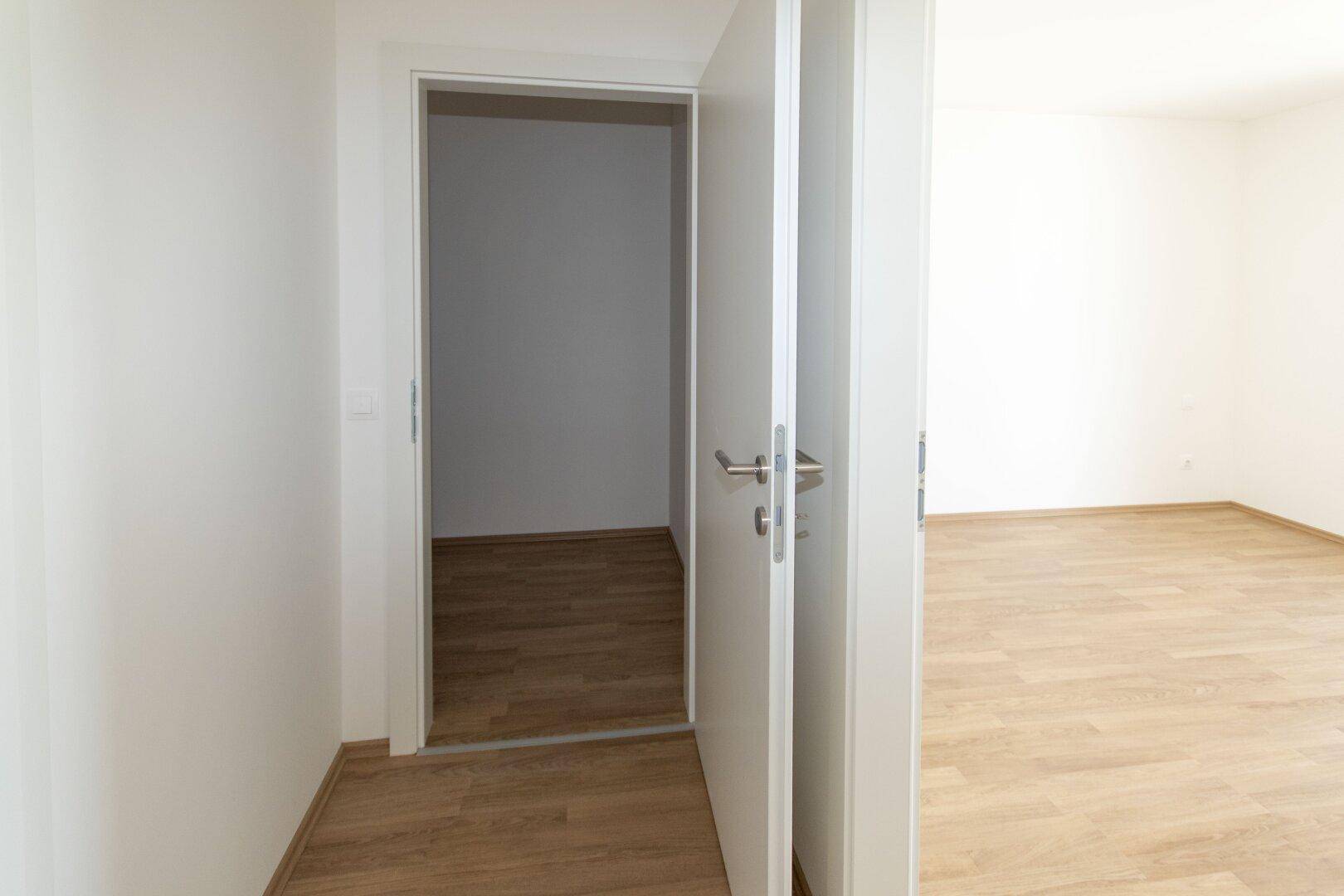 Offene Tür verbindet zwei helle Räume mit durchgehendem Holzboden.