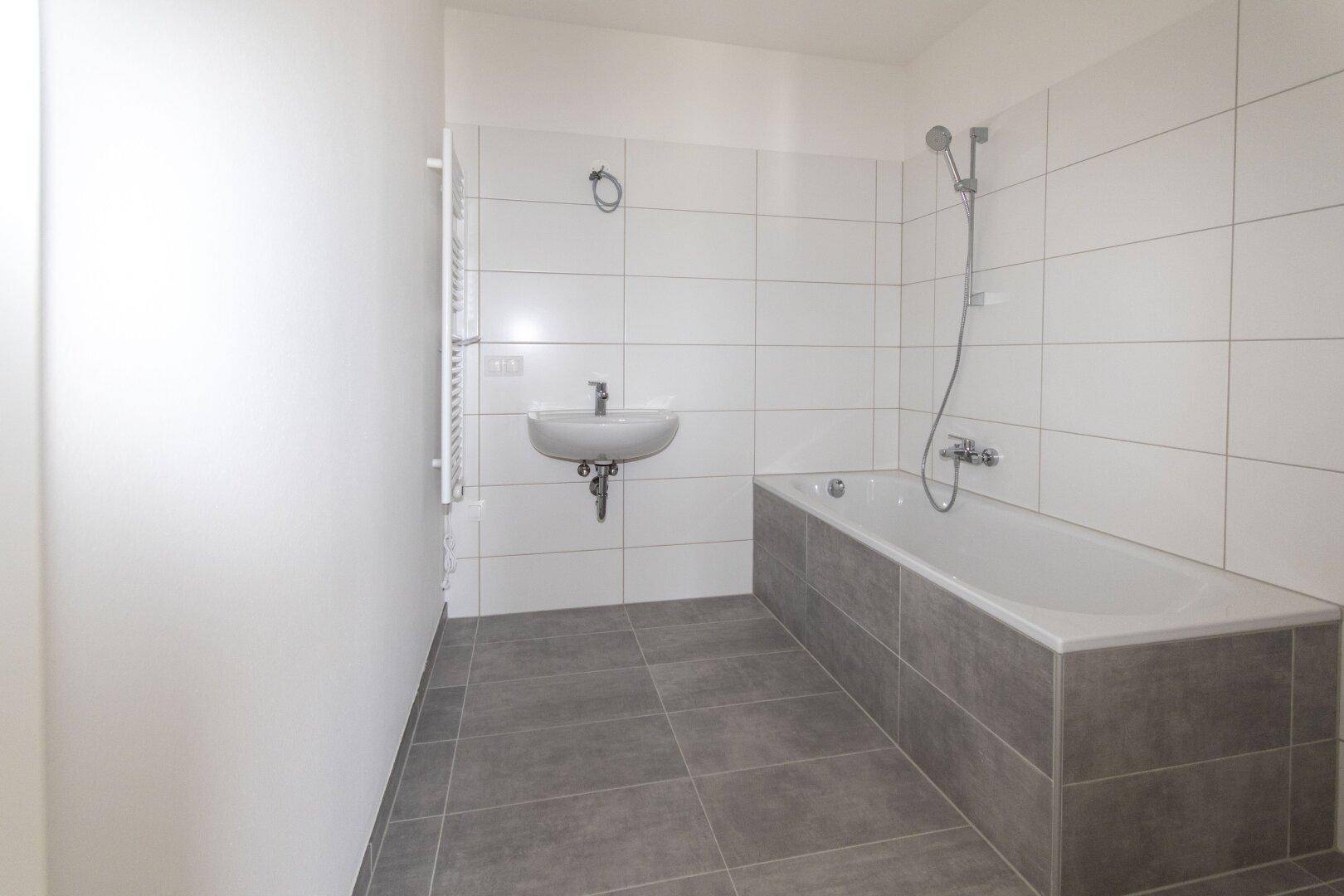 Modernes Badezimmer mit Badewanne, Waschbecken und weißen Wandfliesen sowie Handtuchheizkörper.