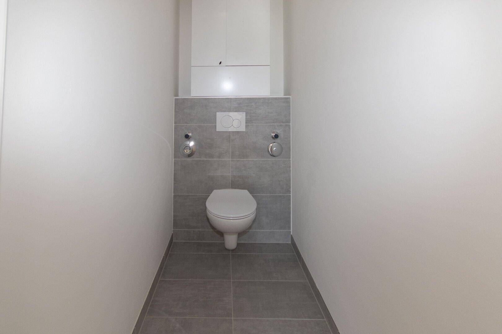 Separates WC mit wandhängender Toilette und modernen grauen Fliesen im Neubau.