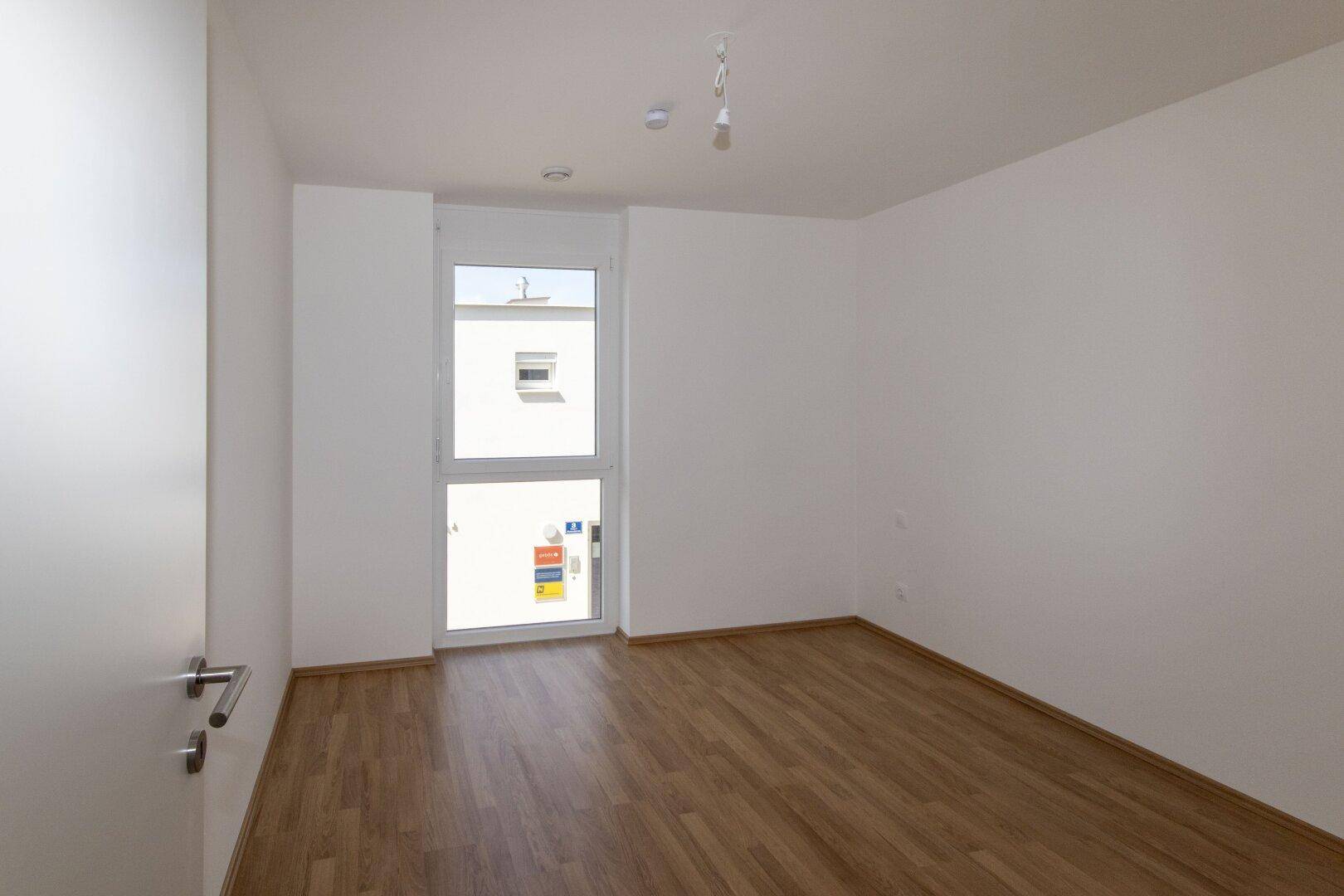 Leeres Schlafzimmer mit Holzboden und Fenster, das einen Blick nach draußen bietet.
