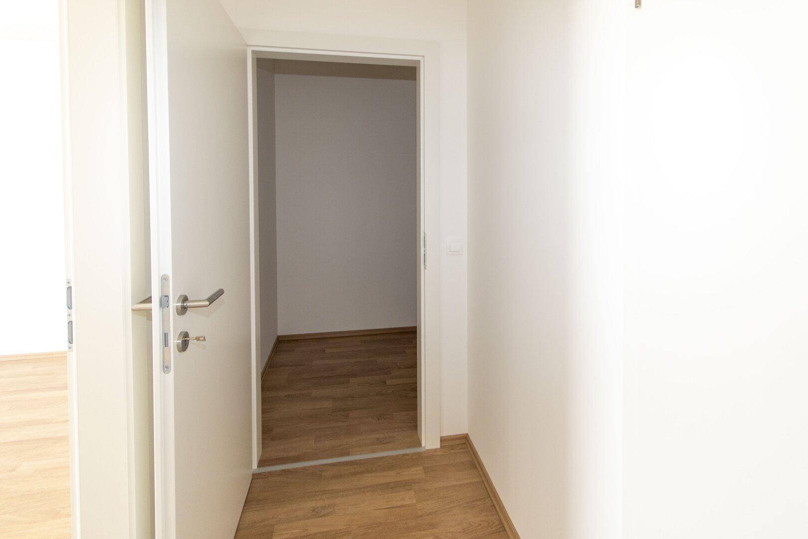 Heller Flur mit Holzboden und offener Tür, die zu einem weiteren Raum führt.