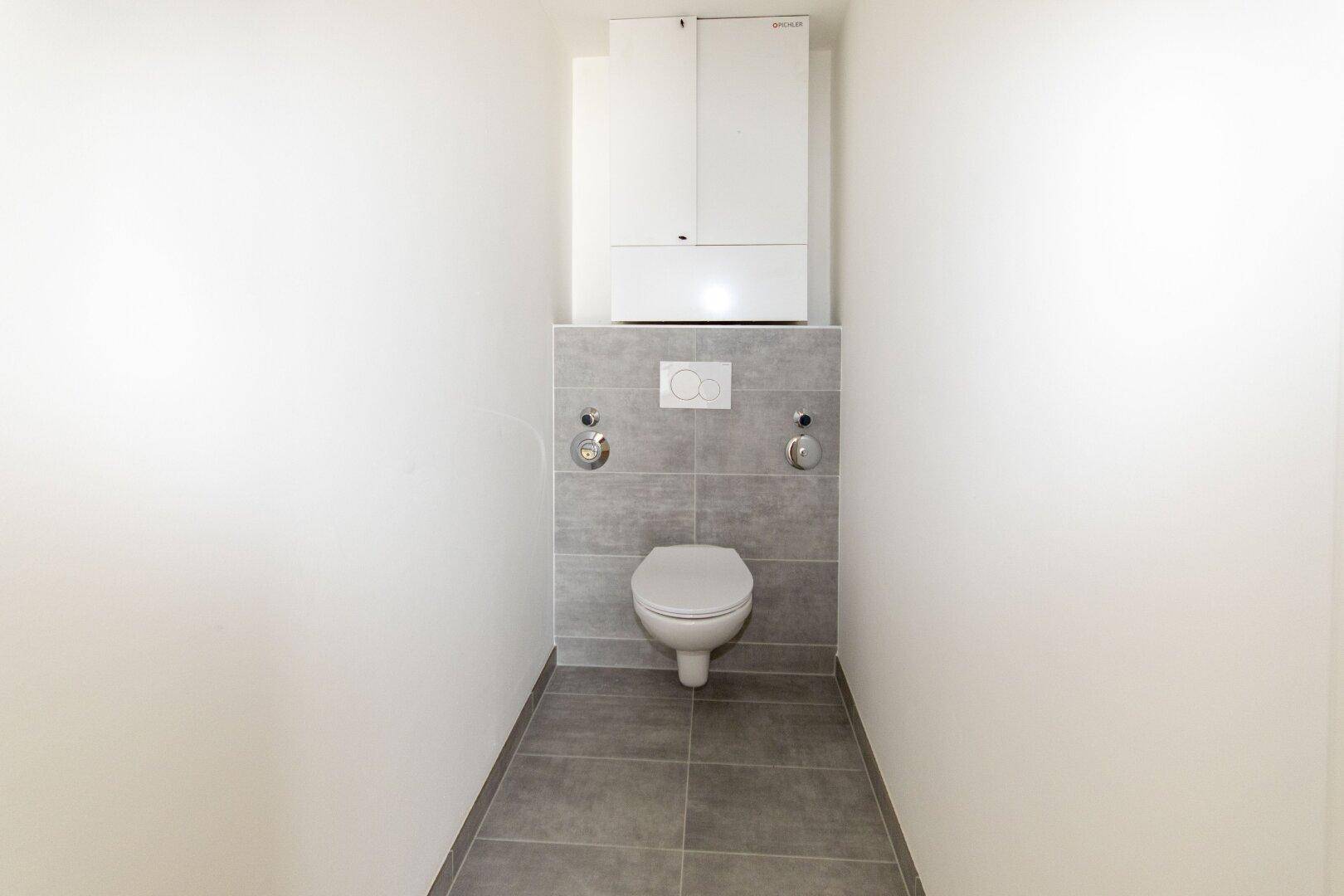 Separates WC mit Wand-WC und modernen grauen Fliesen.