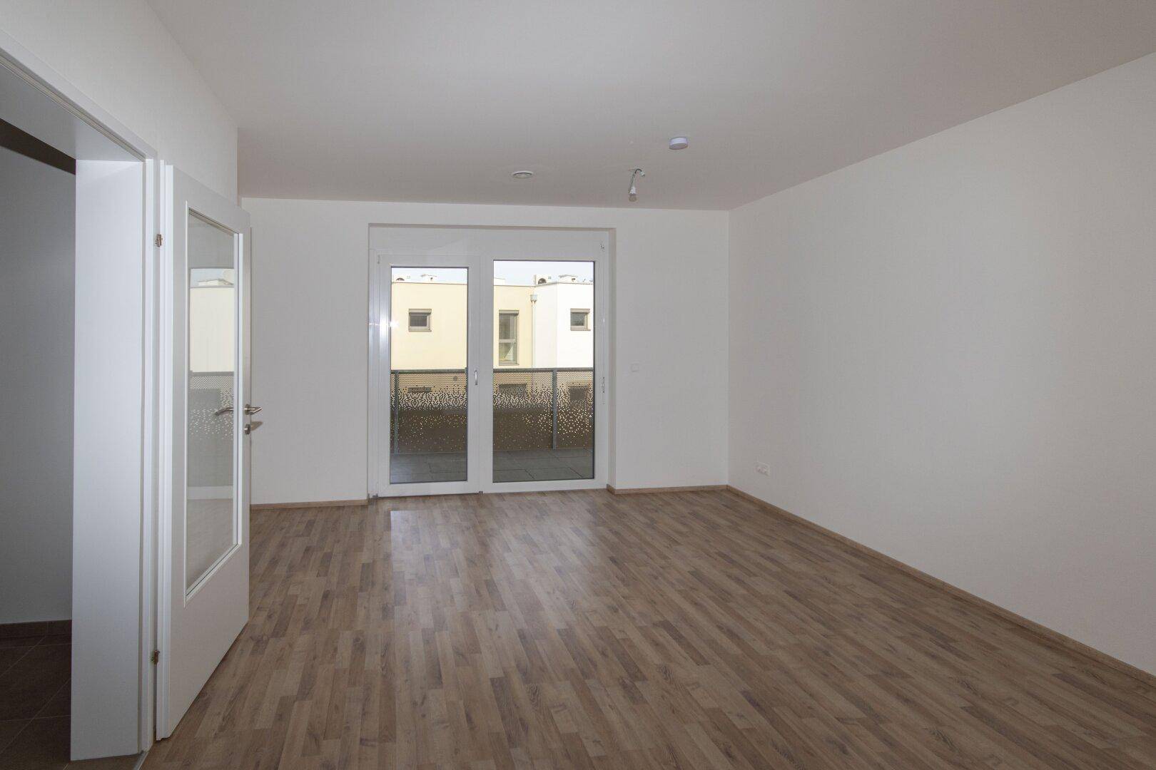 Heller, leerer Raum mit Holzboden und Zugang zu einem Balkon.