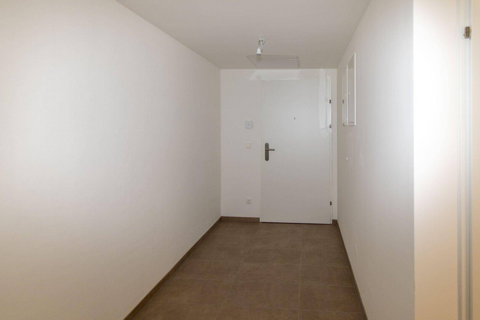 Heller Eingangsbereich mit braunen Fliesen und weißer Wohnungstür.