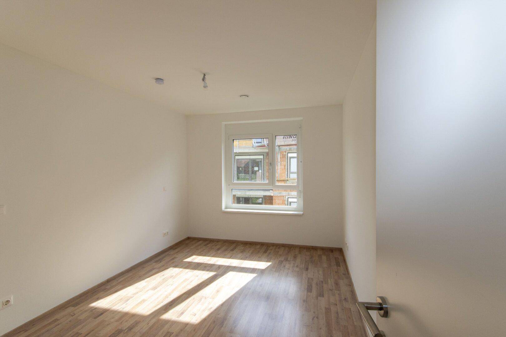 Leeres Schlafzimmer mit hellem Laminatboden und weiß gestrichenen Wänden.