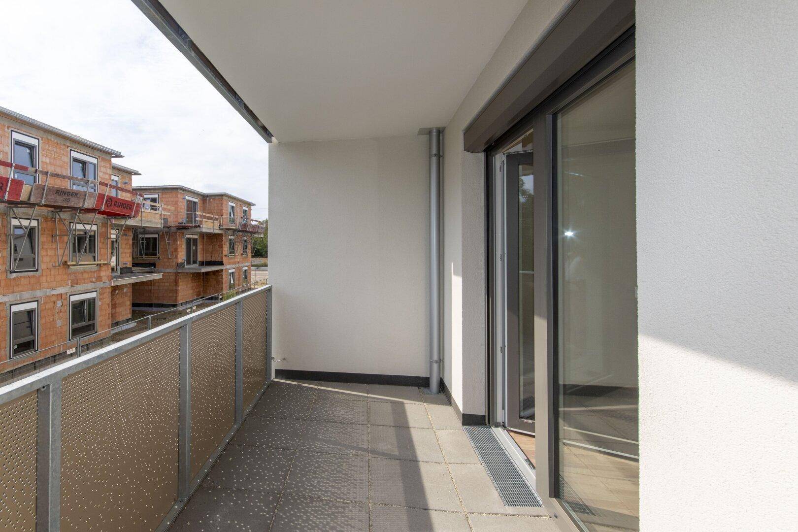 Moderner Balkon mit Fliesenboden und Blick auf die umliegenden Neubauten.