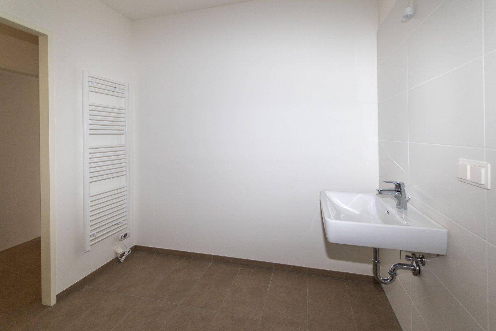 Helles Badezimmer mit Einzelwaschbecken, weißen Fliesen und beheiztem Handtuchhalter.