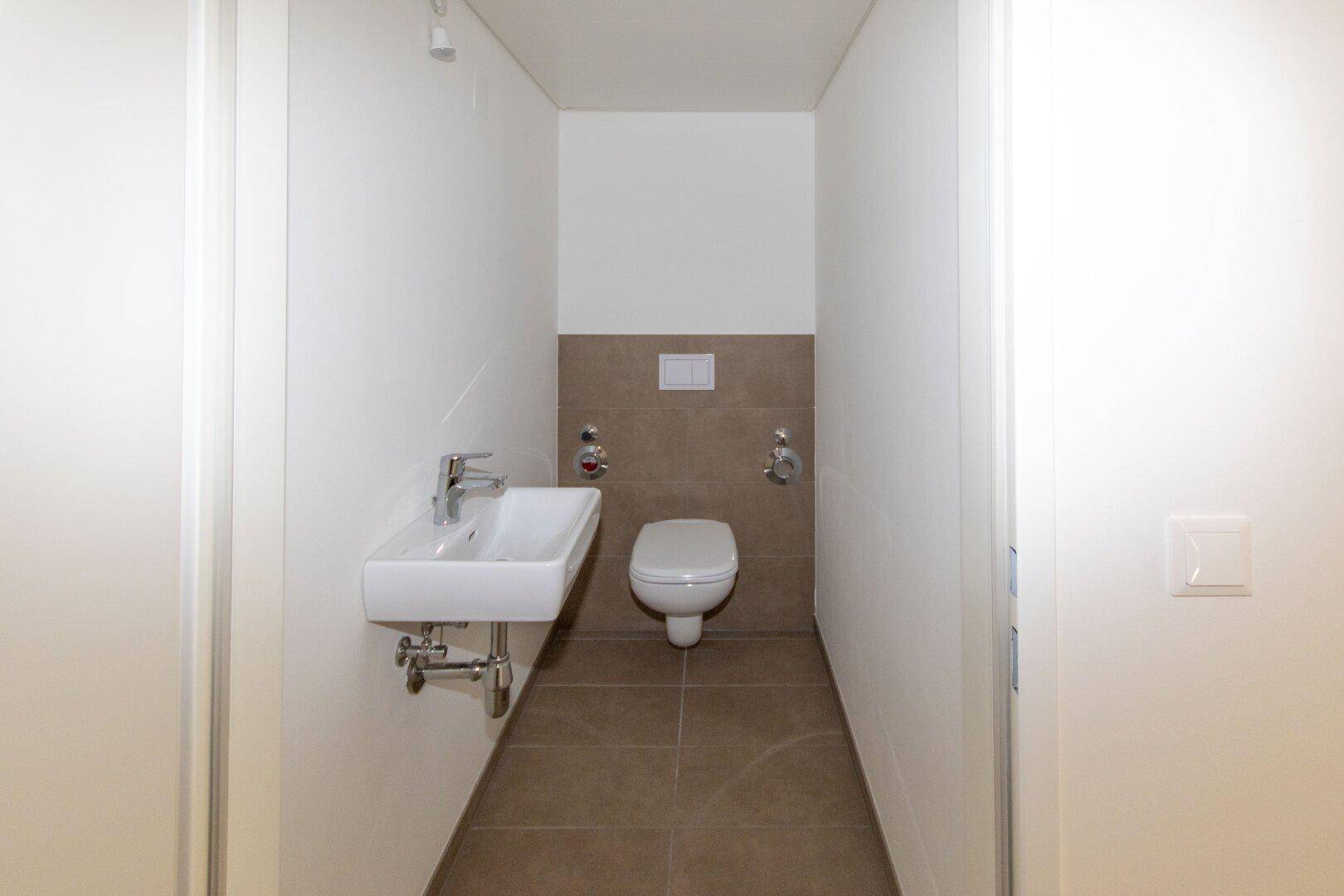 Kleines Gäste-WC mit Wand-WC, Einzelwaschbecken und teilweisen Wandfliesen.