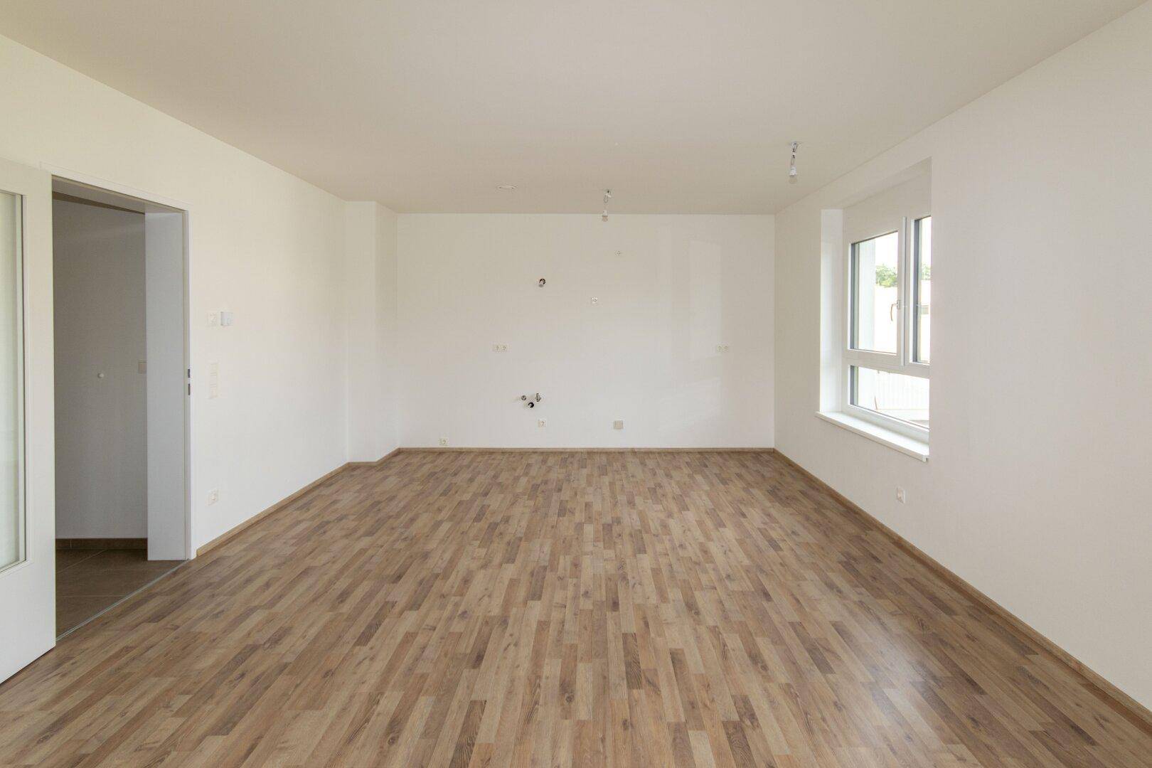 Leerer Raum mit hellem Laminatboden und weißen Wänden, bereit für individuelle Gestaltung.