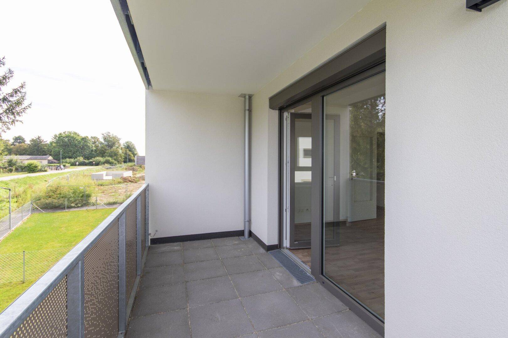 Funktionaler Balkon mit Fliesenboden und Zugang zum Innenbereich durch eine große Glasschiebetür.