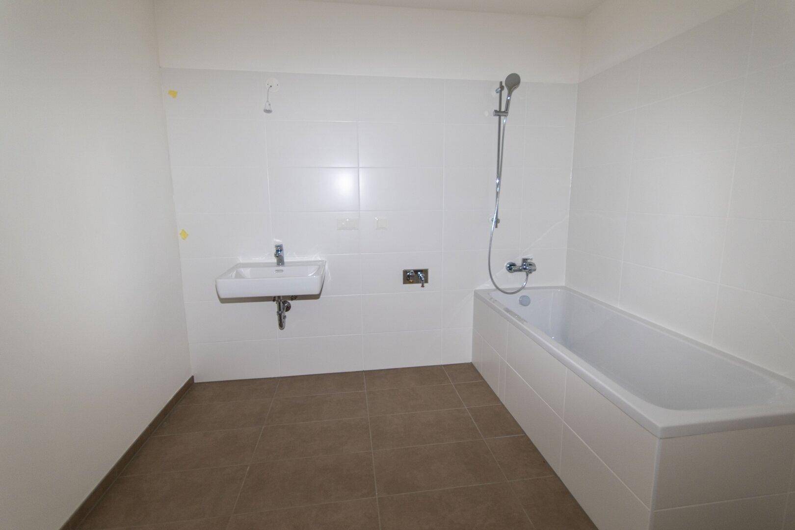 Modernes Badezimmer mit weiß gefliesten Wänden, einer Badewanne und einem einzelnen Waschbecken.
