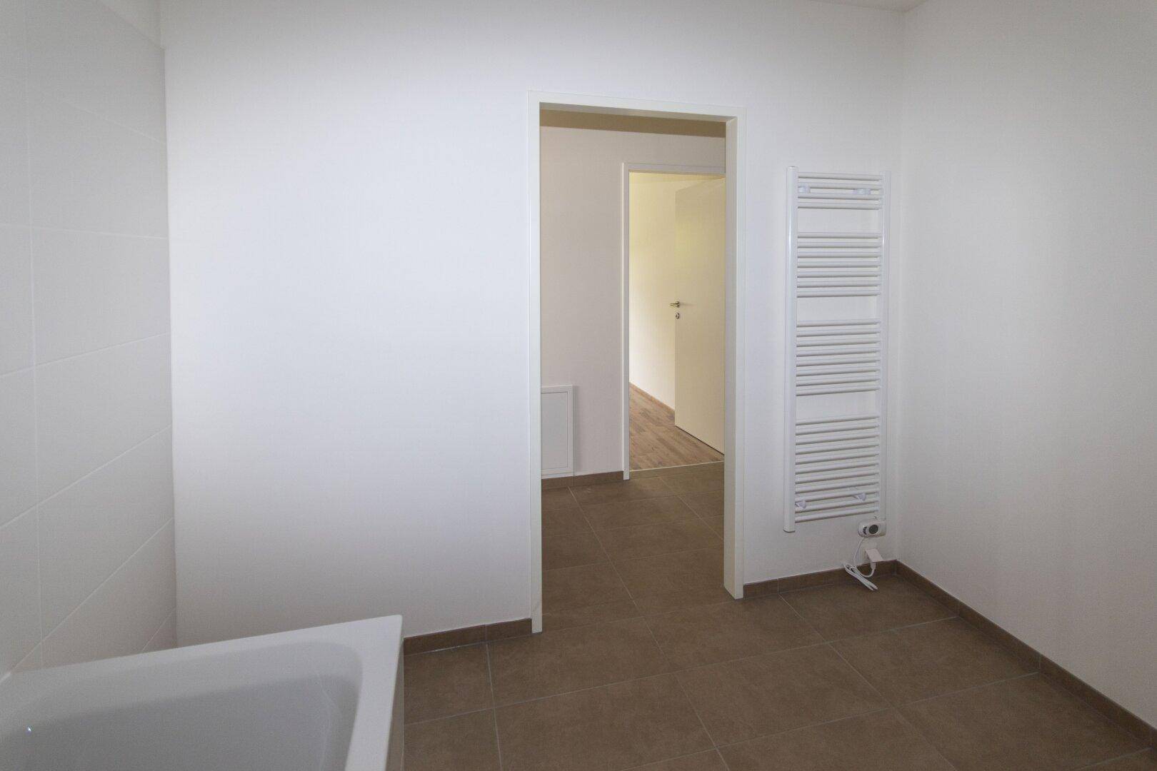 Funktionales Badezimmer mit Fliesenboden, weiß gefliesten Wänden und einem praktischen Handtuchheizkörper.
