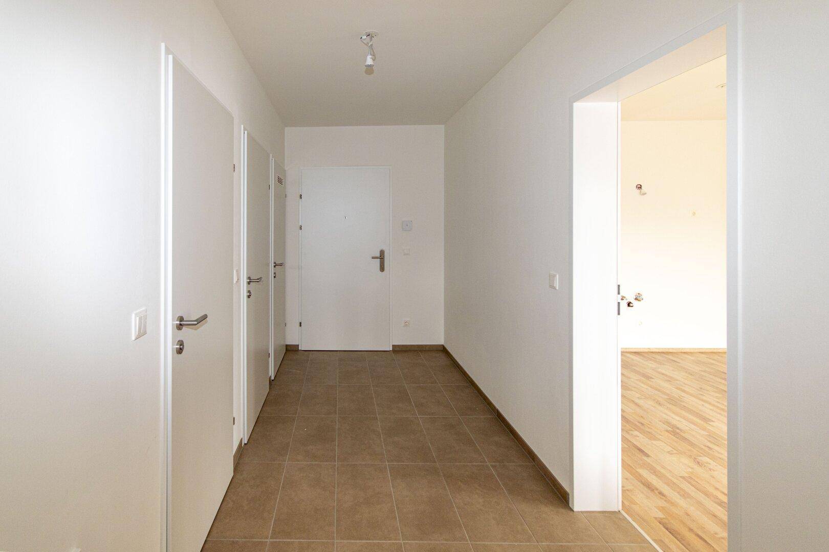 Heller Flur mit braunen Fliesen und mehreren Türen, der verschiedene Räume der Wohnung verbindet.