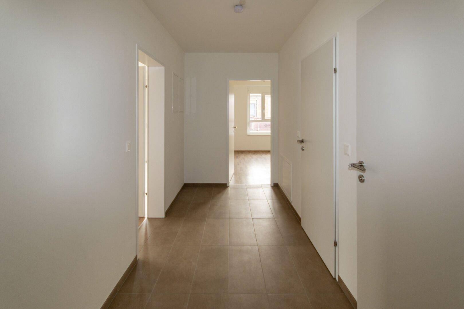 Langer, heller Flur mit Fliesenboden, der zu weiteren Zimmern und einem Fenster am Ende führt.