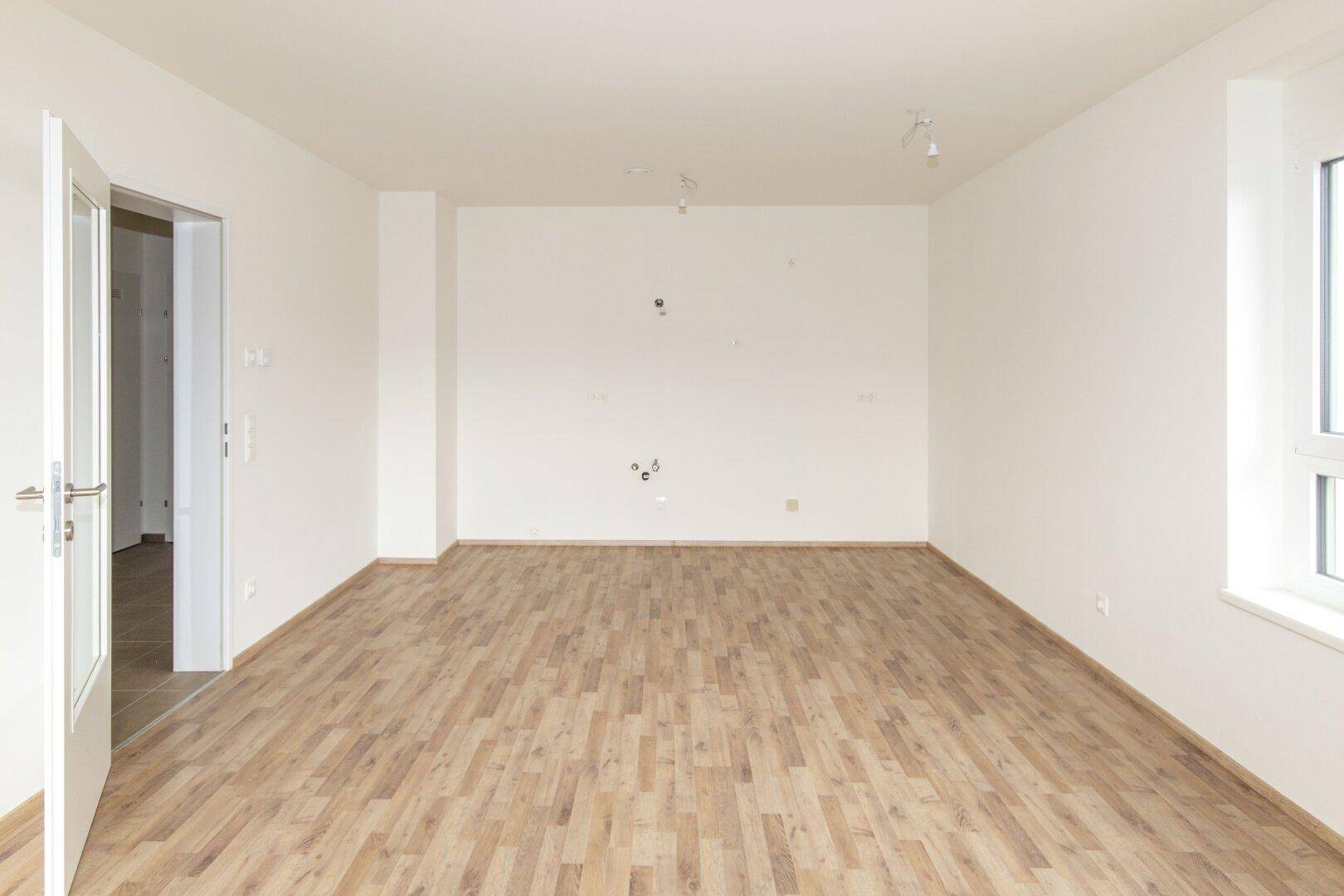 Geräumiges, helles Wohnzimmer mit Laminatboden und weißen Wänden, ideal für moderne Einrichtungskonzepte.