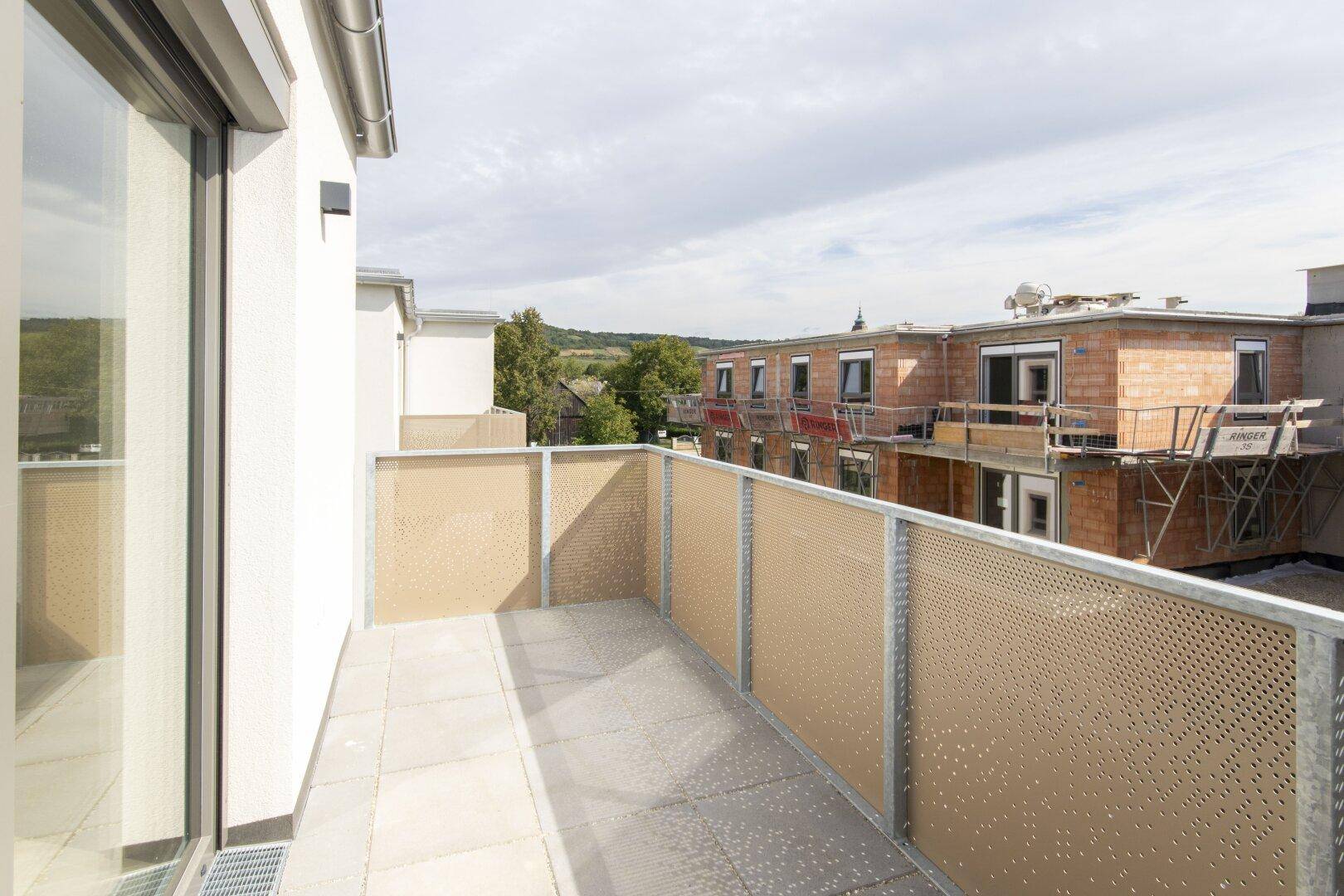 Moderner Balkon mit perforierter Brüstung und Fliesenboden, bietet einen Blick auf die Umgebung.