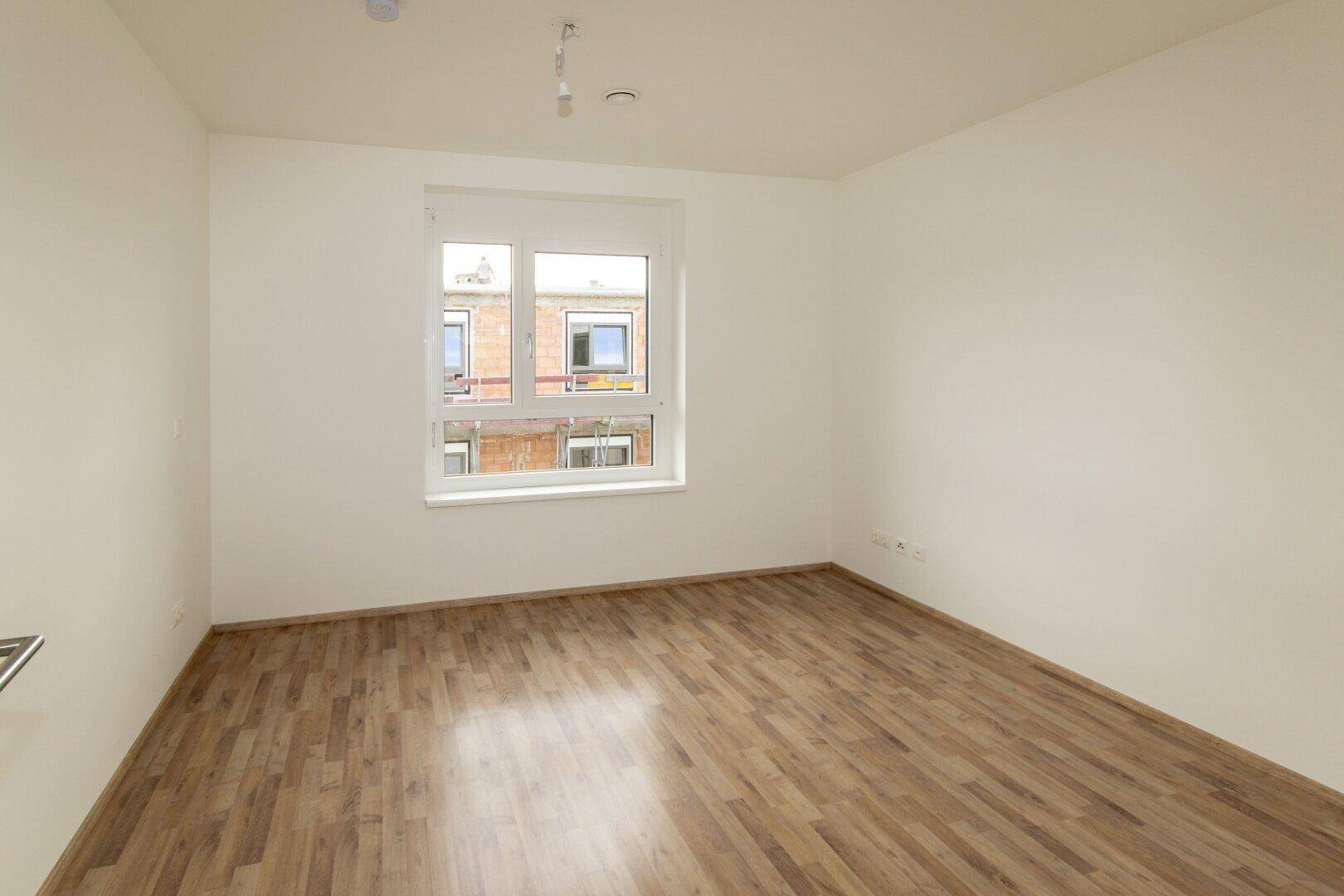 Helles Schlafzimmer mit Laminatboden und großem Fenster, bietet viel Tageslicht und eine angenehme Atmosphäre.