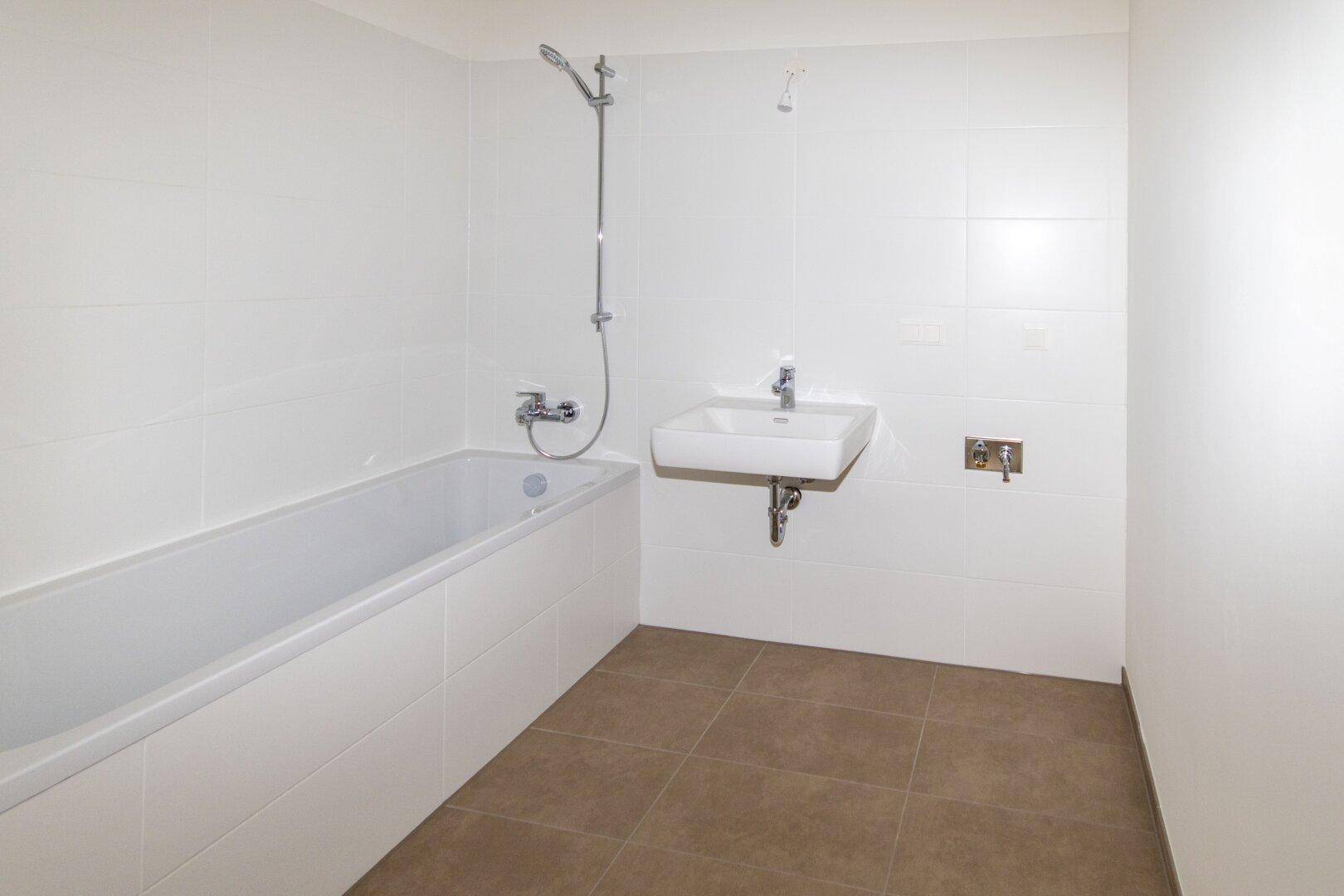 Modernes Badezimmer mit Badewanne, Waschbecken und weißen Fliesen, bereit für die Installation weiterer Armaturen.