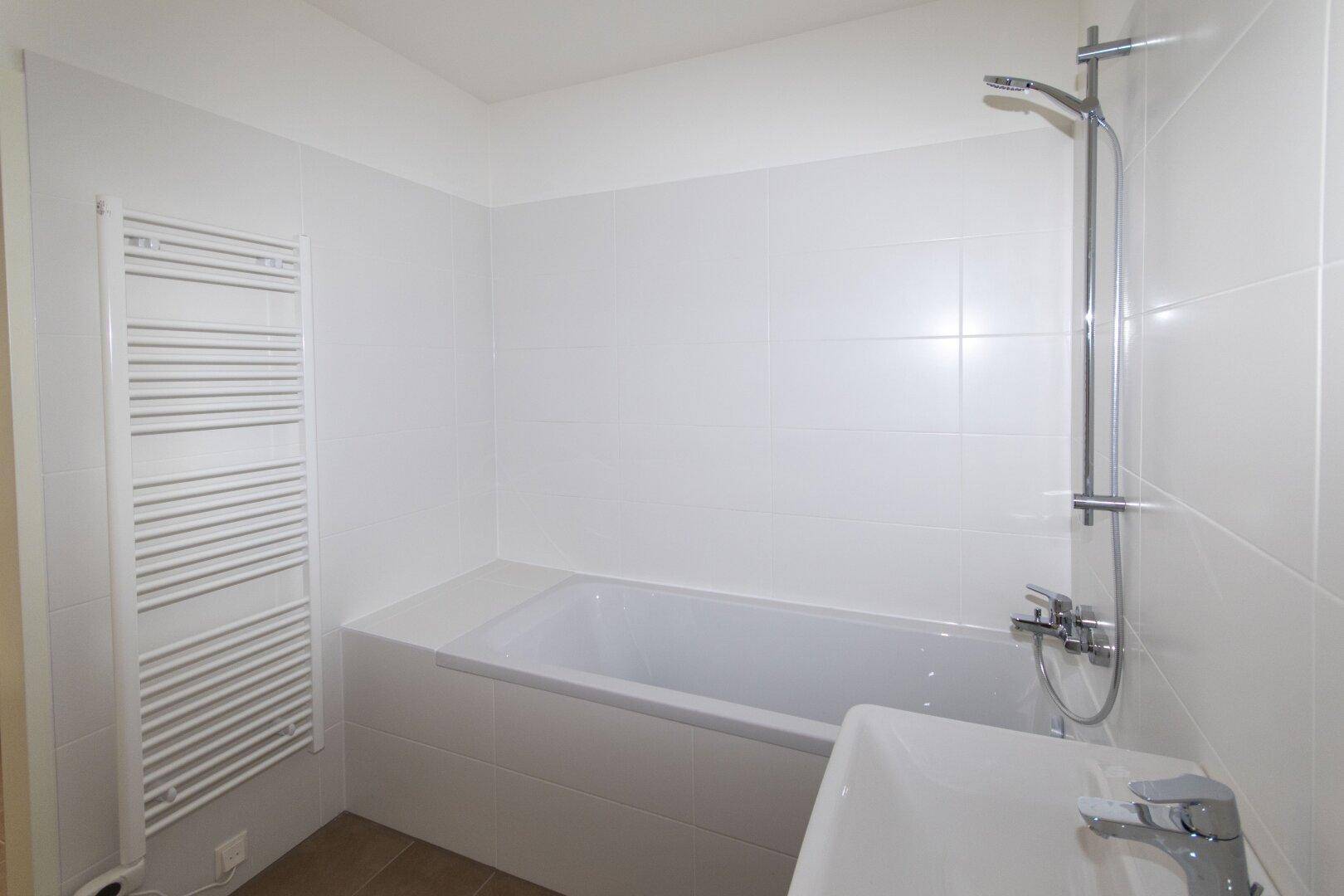 Helles Badezimmer mit Badewanne, Waschbecken und beheiztem Handtuchhalter, komplett gefliest in Weiß.