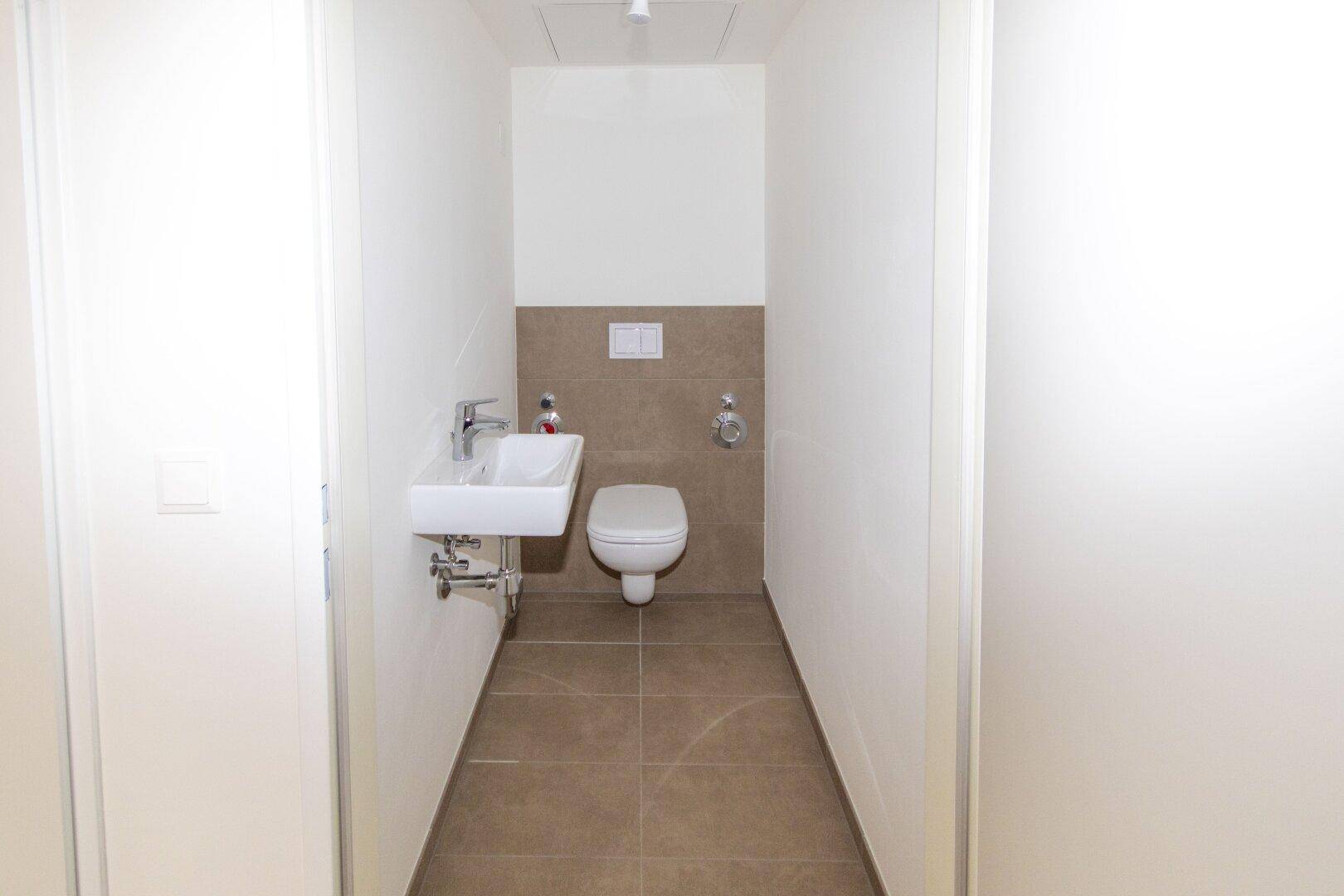 Kompaktes Gäste-WC mit wandhängender Toilette und kleinem Waschbecken, modern gefliest.