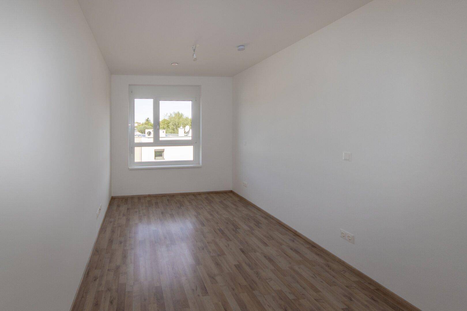 Helles Schlafzimmer mit Laminatboden und einem Fenster, das viel Tageslicht hereinlässt.