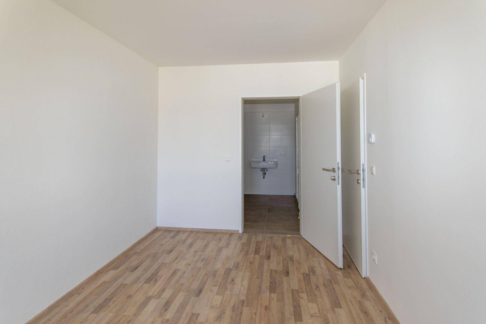 Schlafzimmer mit Laminatboden und direktem Zugang zu einem gefliesten Badezimmer.
