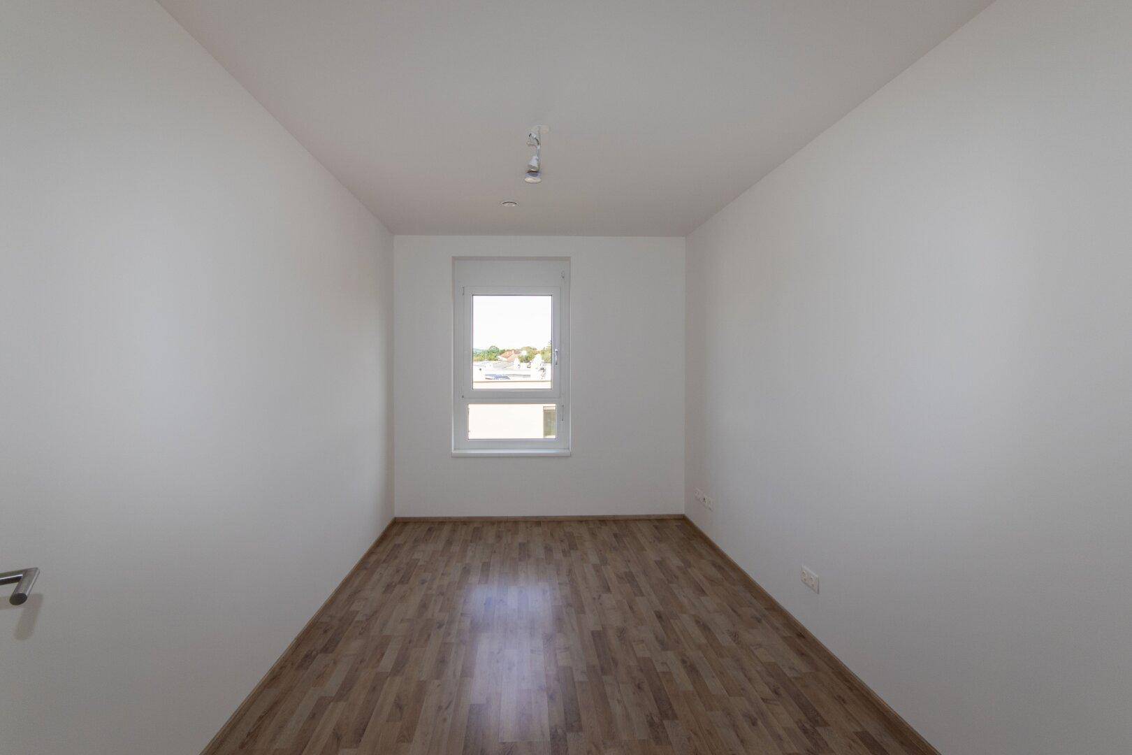 Helles Schlafzimmer mit Laminatboden und einem Fenster, das viel Tageslicht hereinlässt.
