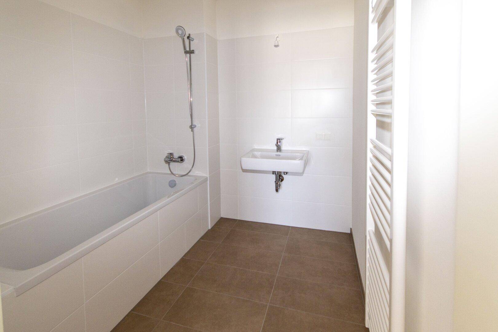 Modernes Badezimmer mit Badewanne, Waschbecken und beheiztem Handtuchhalter, komplett gefliest.