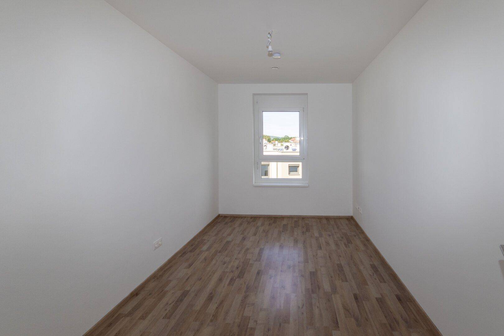 Unmöbliertes Schlafzimmer mit Laminatboden und einem großen Fenster, ideal für individuelle Gestaltung.