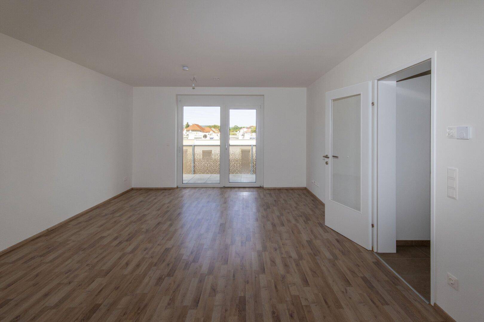 Geräumiges Wohnzimmer mit Laminatboden und Zugang zu einem Balkon, hell und unmöbliert.