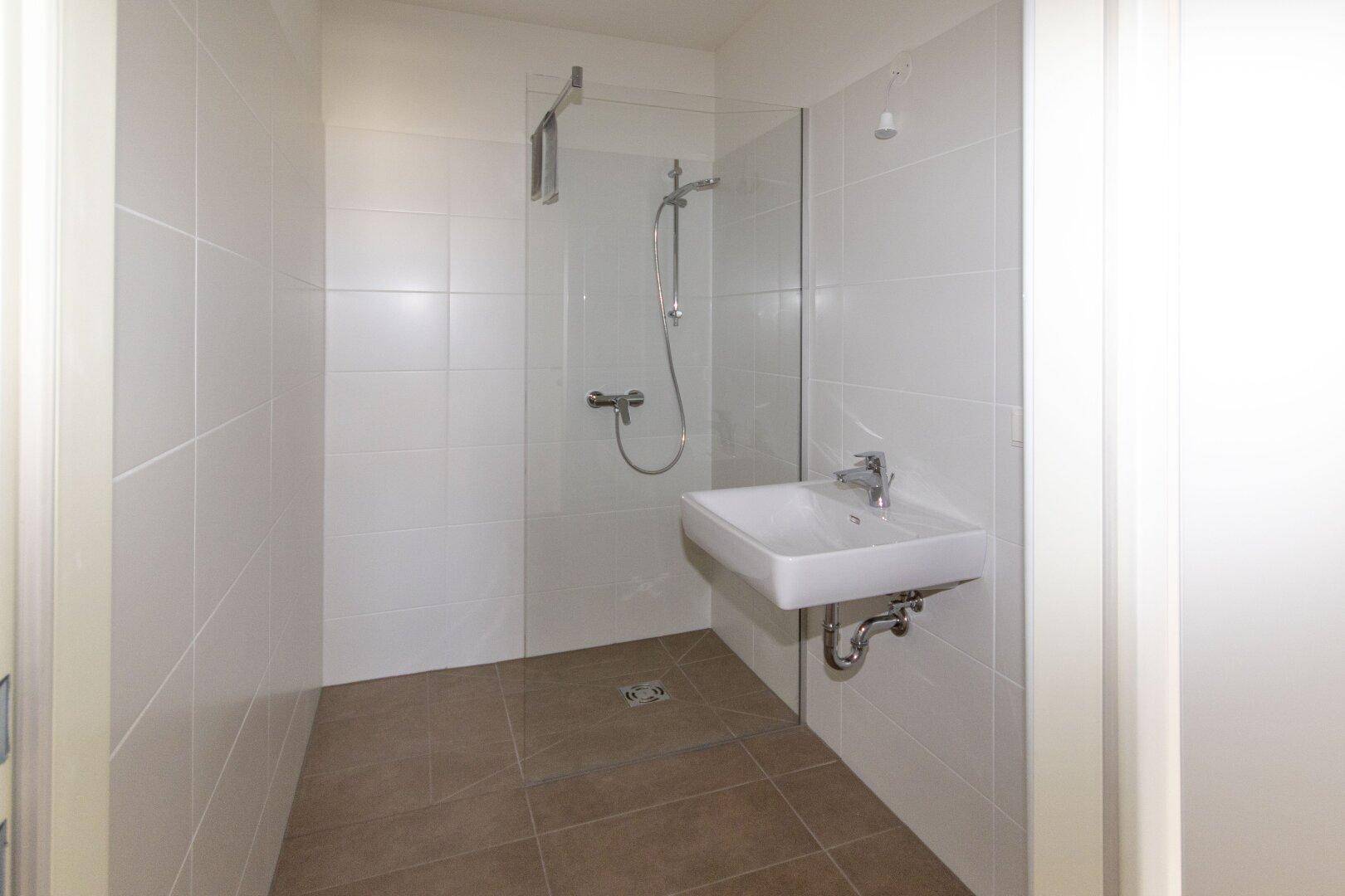 Modernes Badezimmer mit ebenerdiger Dusche und Waschbecken, komplett weiß gefliest.