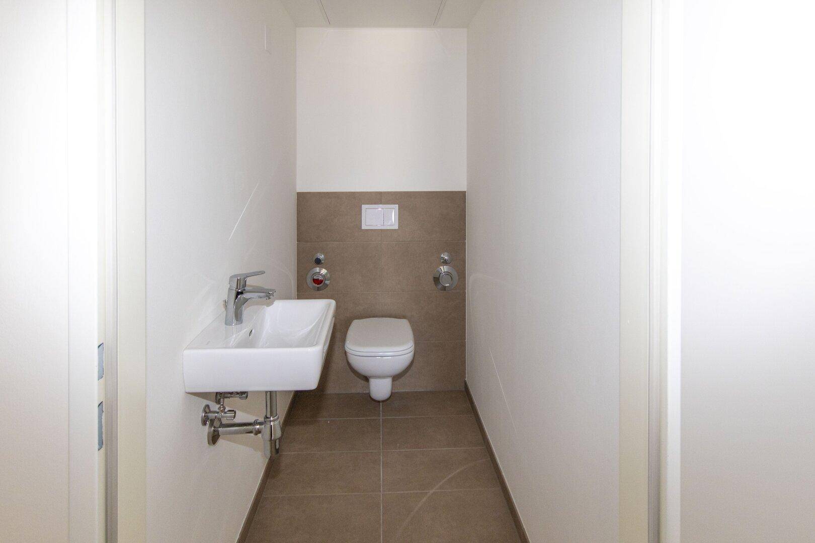 Separates Gäste-WC mit wandhängender Toilette und kleinem Waschbecken, modern gefliest.
