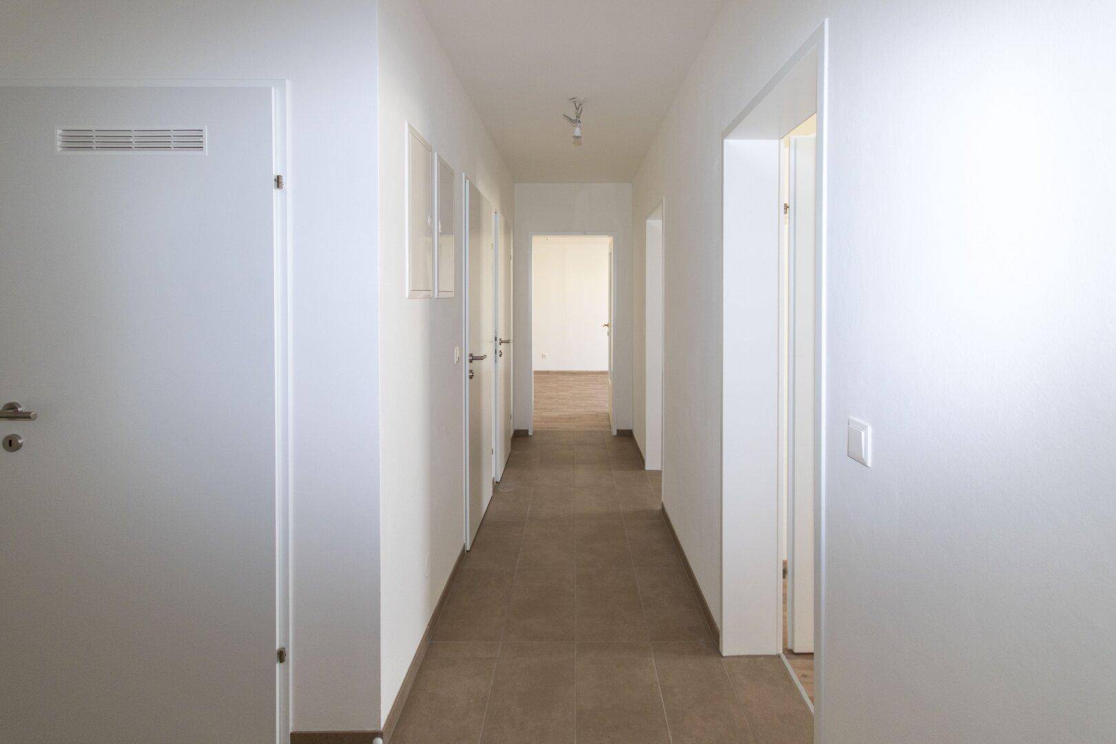 Langer, heller Flur mit Fliesenboden, der verschiedene Räume der Wohnung verbindet.