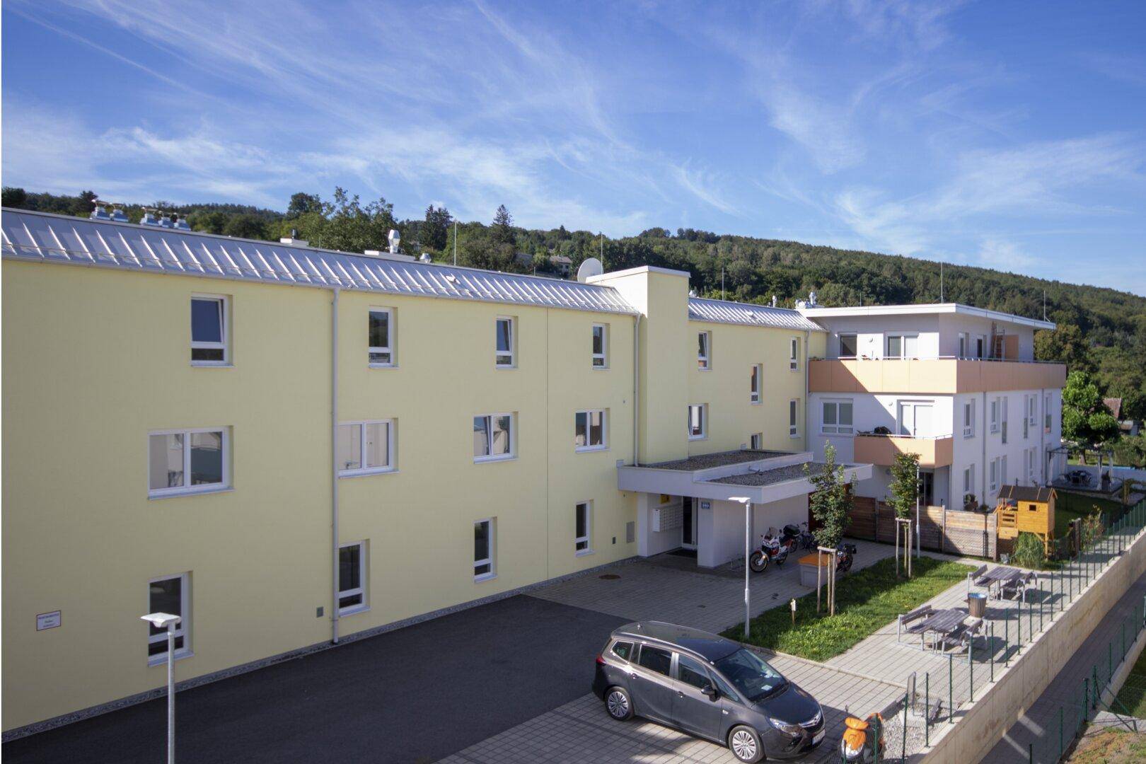 Gesamtanlage des modernen Wohnkomplexes mit Parkplätzen und Außenbereich mit Sitzgelegenheiten.