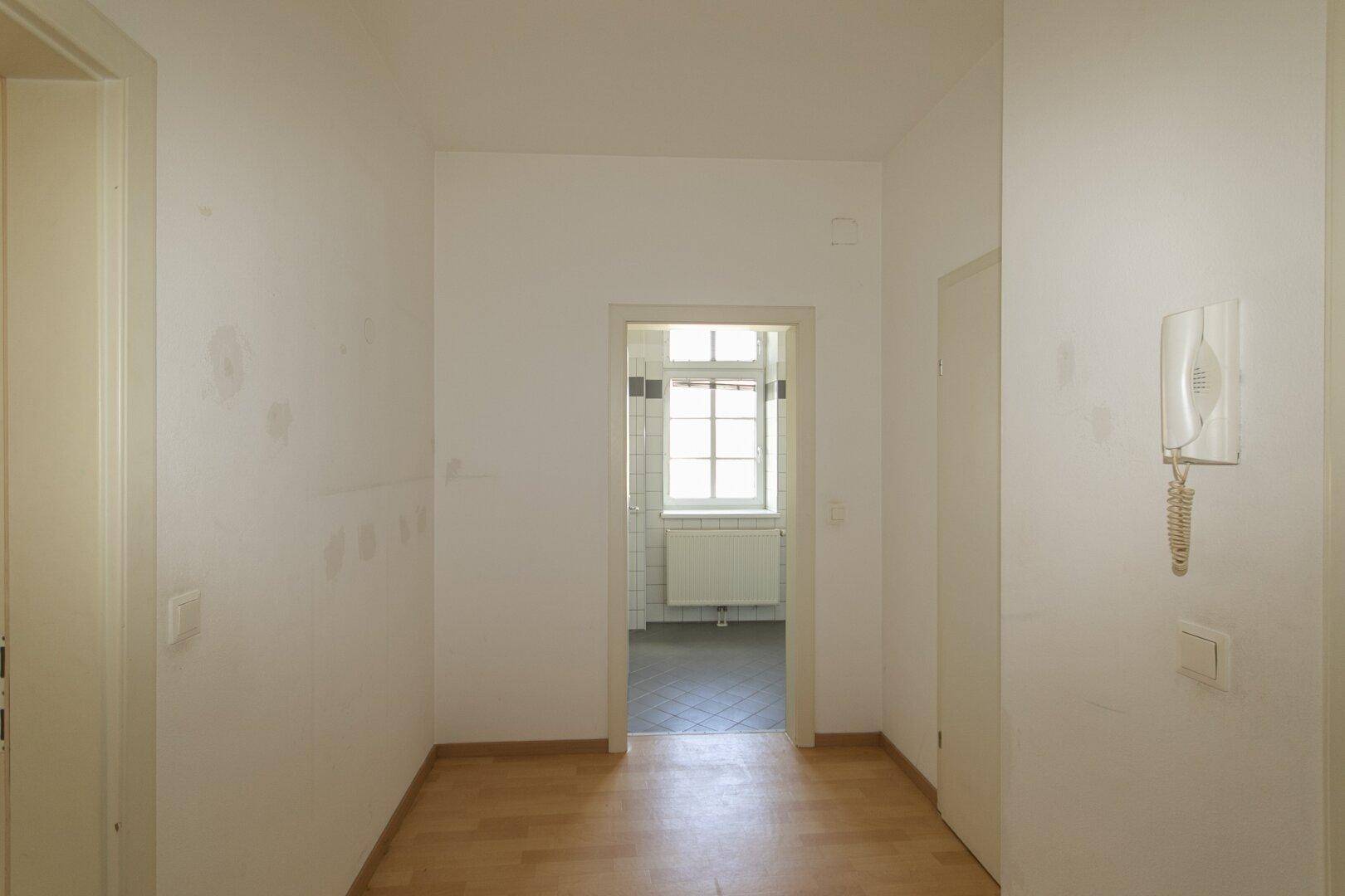 Heller Flur mit Holzfußboden und Blick in ein gefliestes Badezimmer.