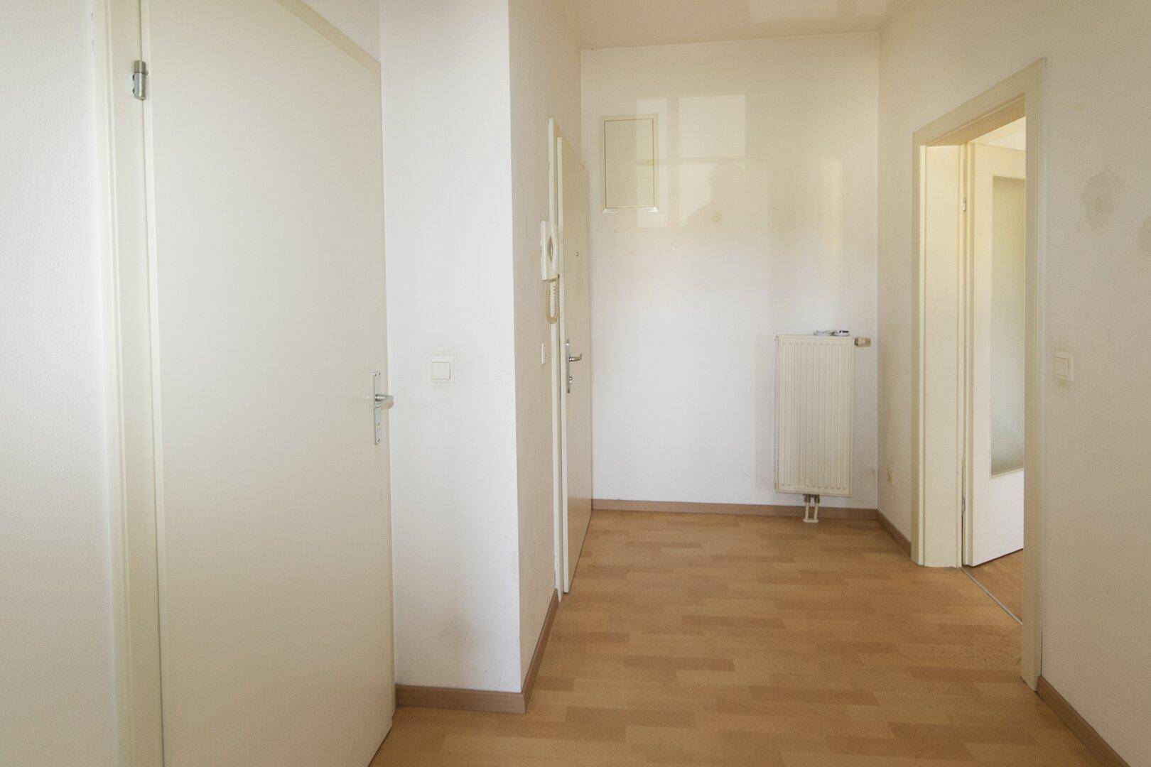 Langer, heller Flur mit Parkettboden, Gegensprechanlage und Heizkörper.