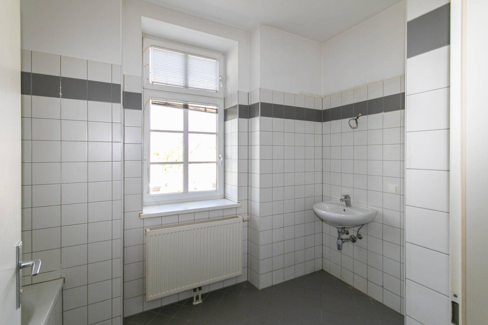 Gefliestes Badezimmer mit Waschbecken, Fenster und Heizkörper, in gutem Zustand.