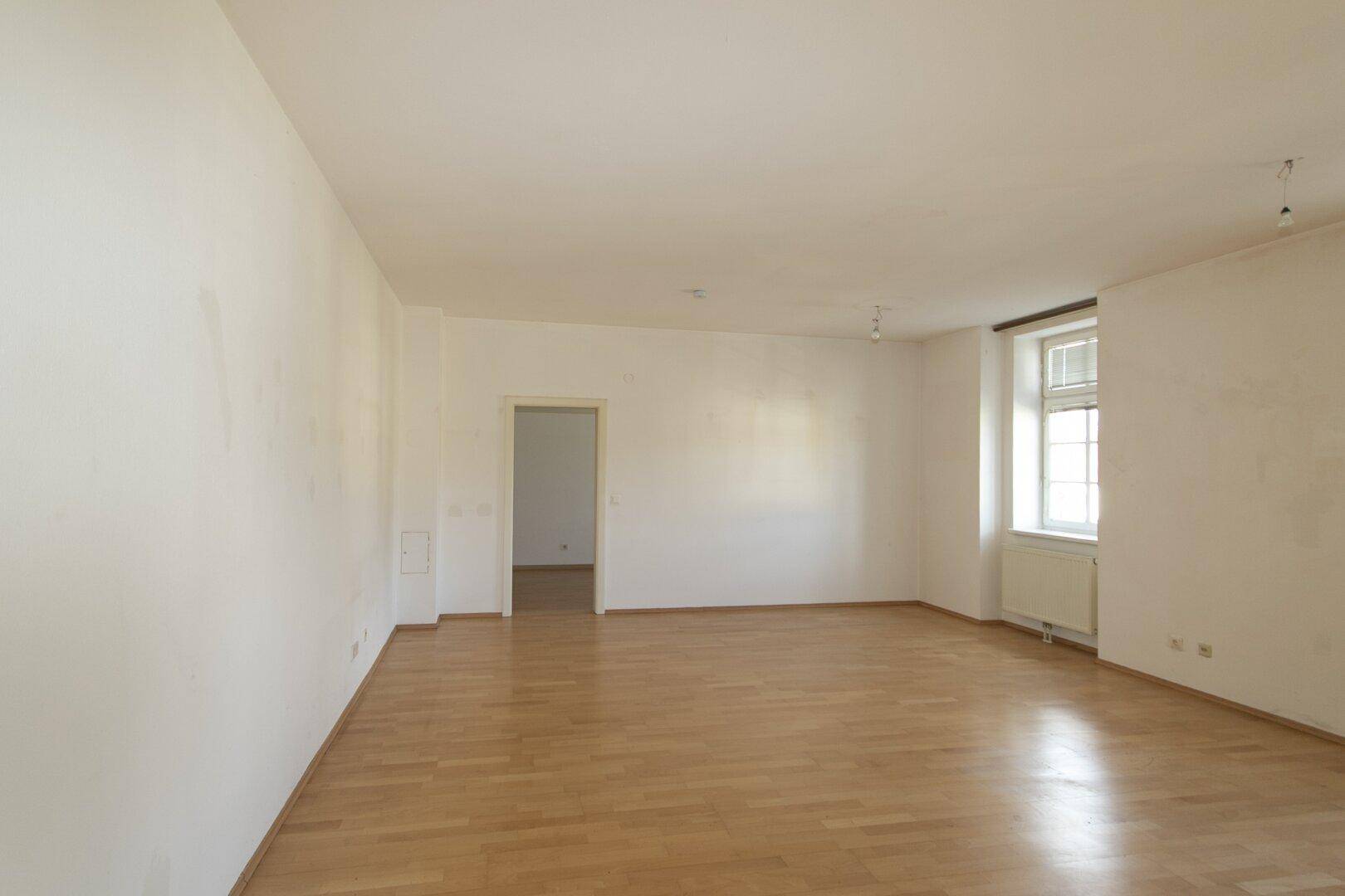 Geräumiges, helles Zimmer mit Parkettboden und Zugang zu weiteren Räumen.