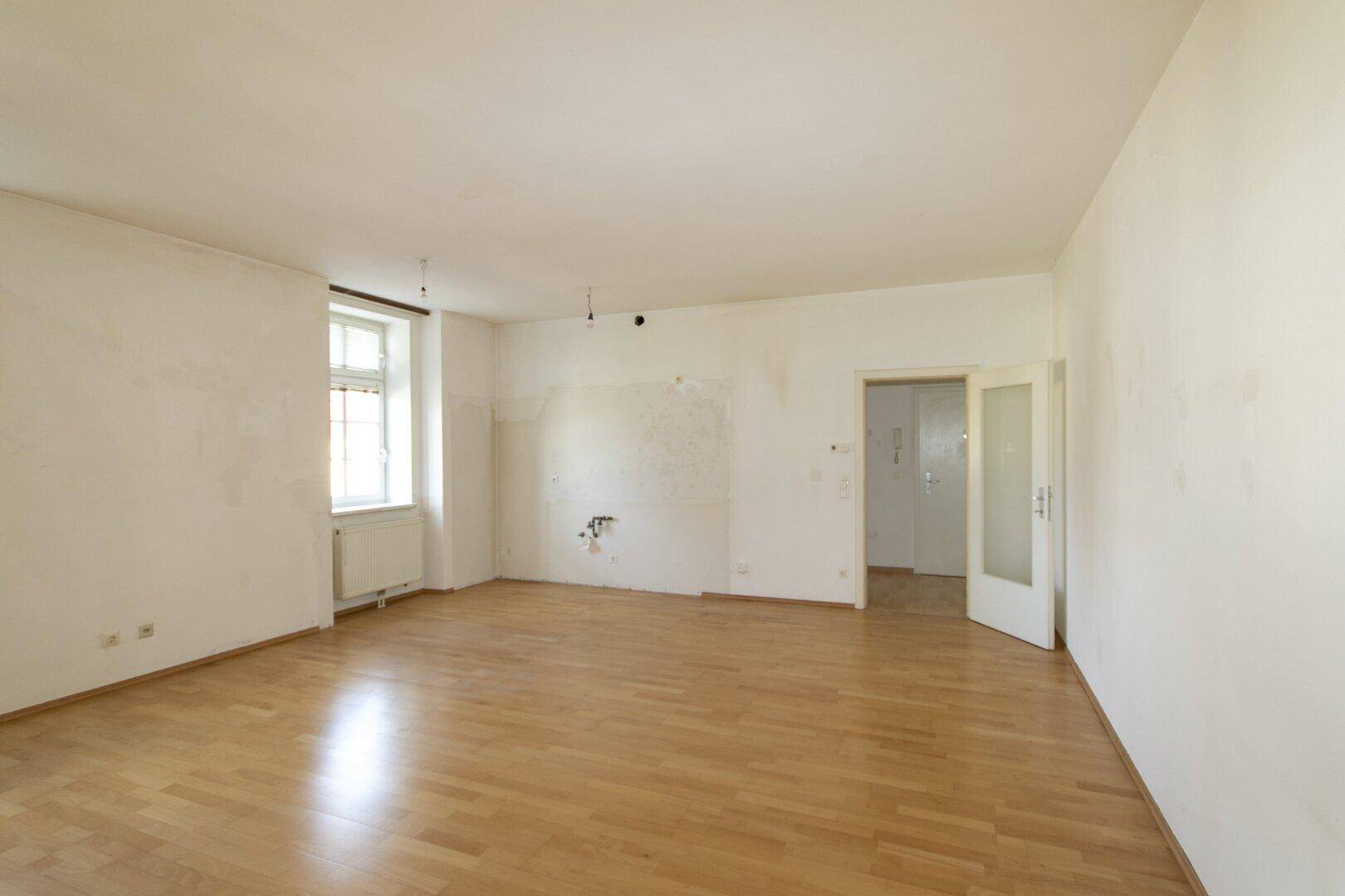 Großes, helles Zimmer mit Parkettboden und Doppeltür zu einem angrenzenden Bereich.
