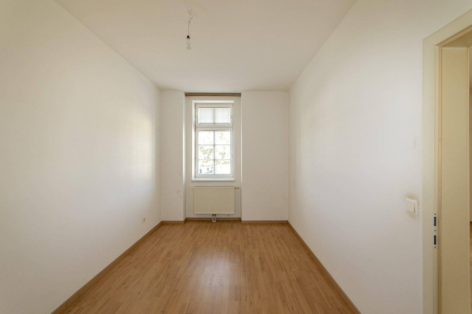 Helles, schmales Zimmer mit Holzfußboden und einem Fenster, ideal als Schlafzimmer.