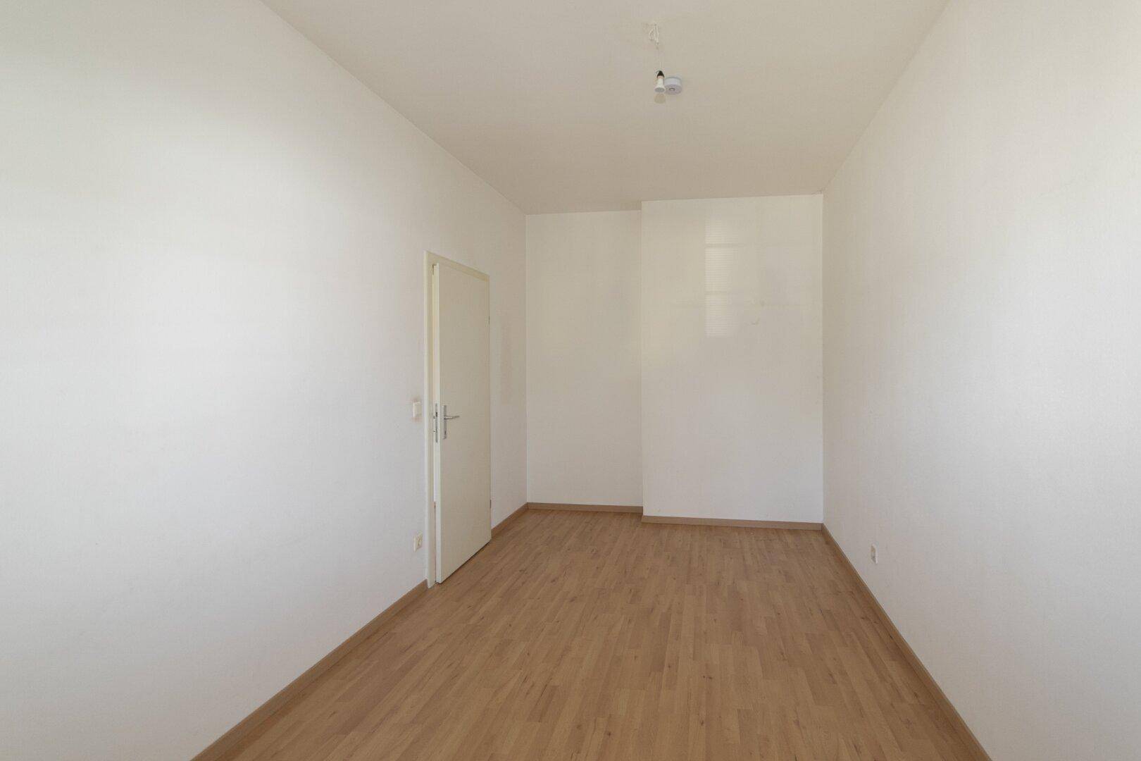 Leeres Zimmer mit Parkettboden und weißer Tür, bereit zur Einrichtung.