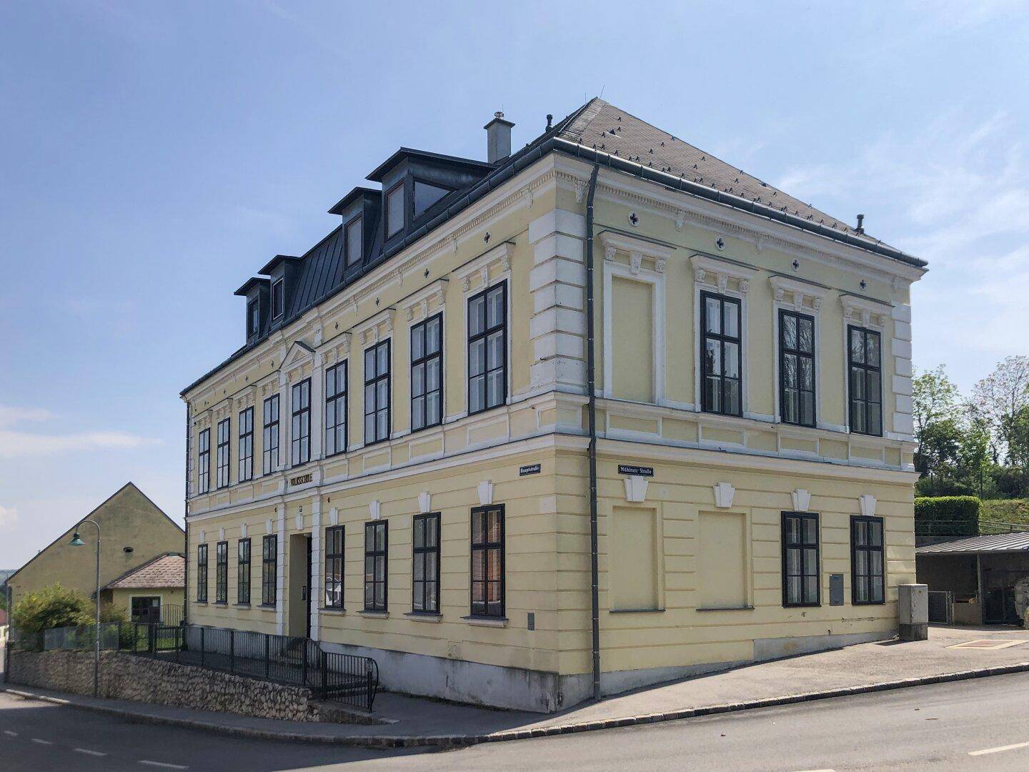 Historisches Eckgebäude mit gelber Fassade und vielen Fenstern unter blauem Himmel.