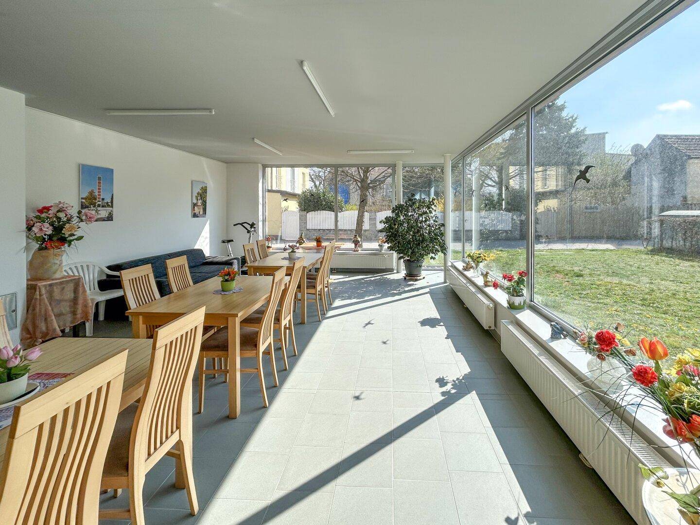 Heller, langer Speisesaal mit großen Fensterfronten, die einen Blick auf den Garten bieten und viel Tageslicht hereinlassen.