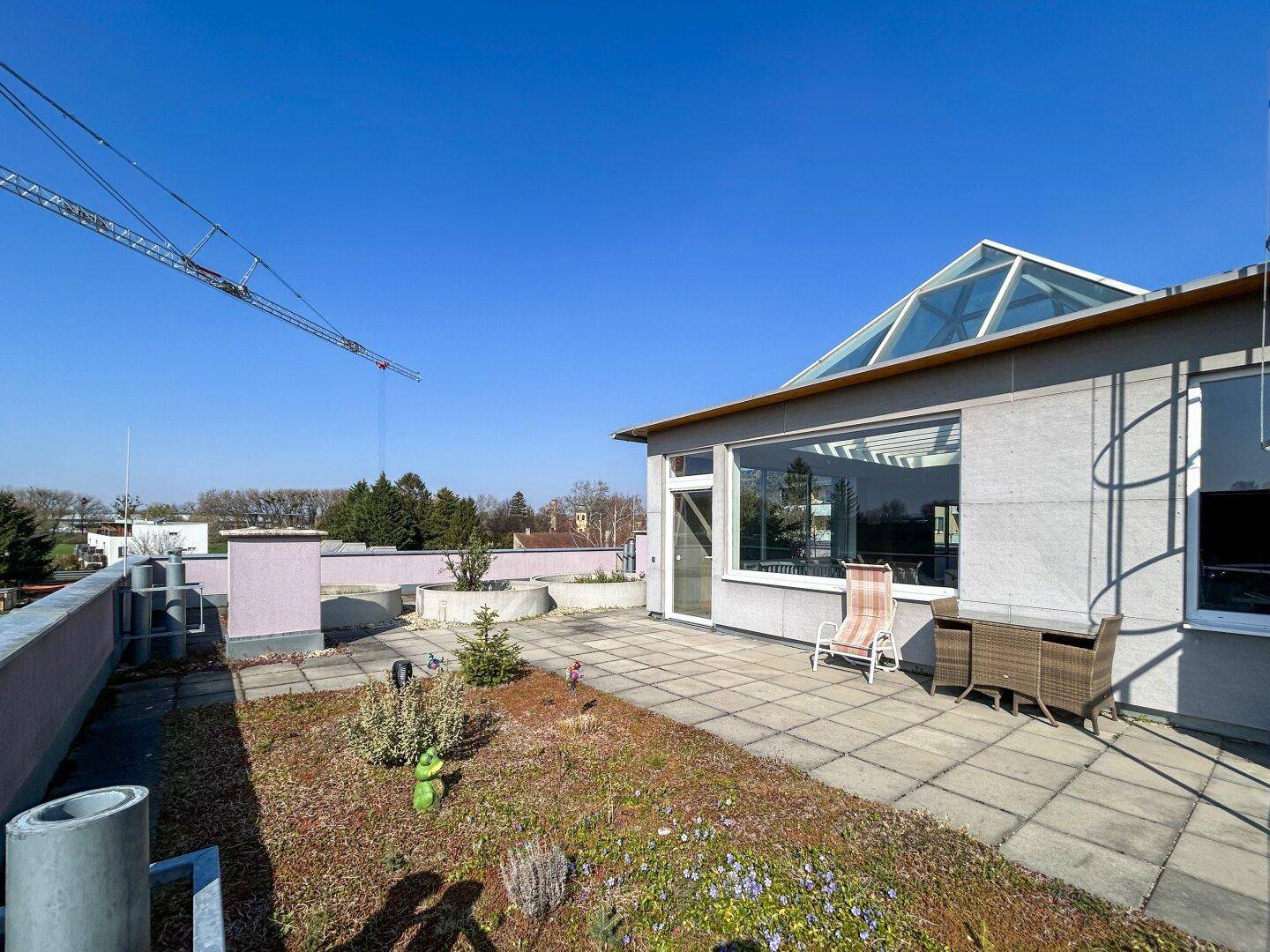 Geräumige Dachterrasse mit begrünter Fläche, Pflastersteinen und einer Glaspyramide, ideal für Entspannung im Freien.