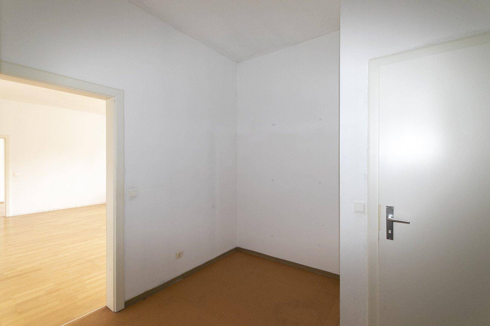 Heller Eckbereich mit Tür und Blick in einen angrenzenden Raum mit Parkettboden.
