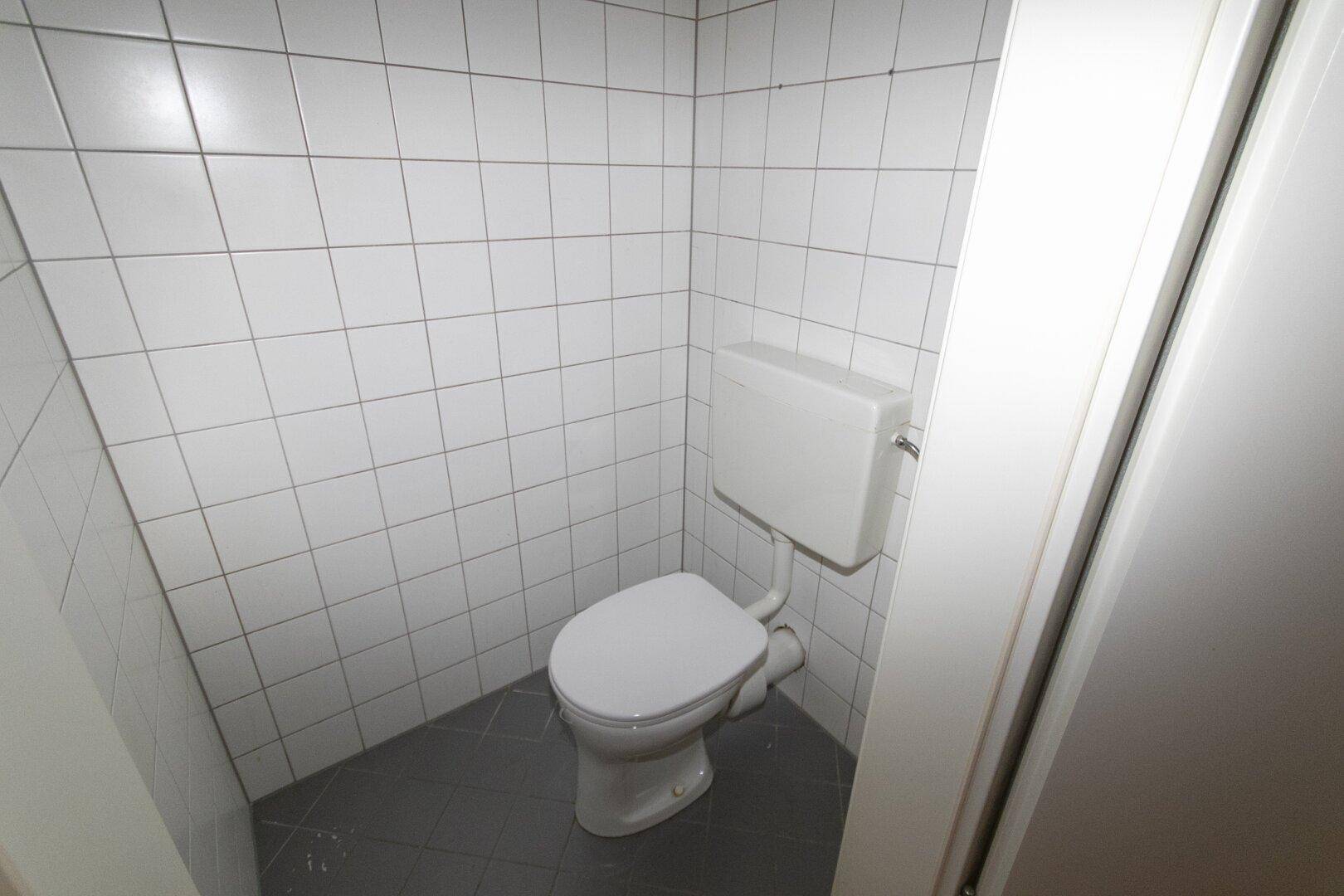 Separates WC mit Toilette und weißen Wandfliesen, funktional und sauber.